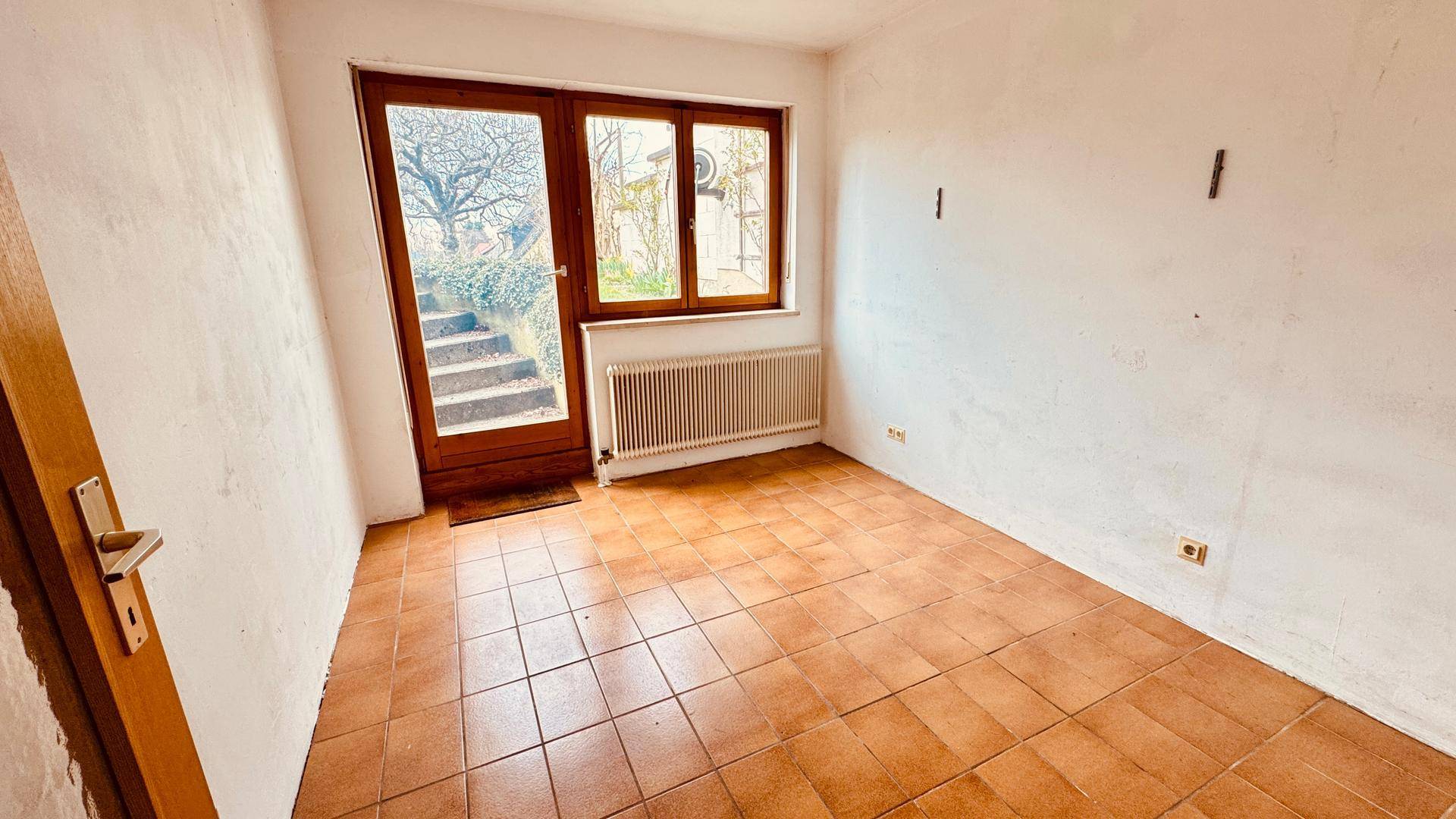 Leeres Zimmer mit Terrakottafliesen und direktem Zugang zum Garten.