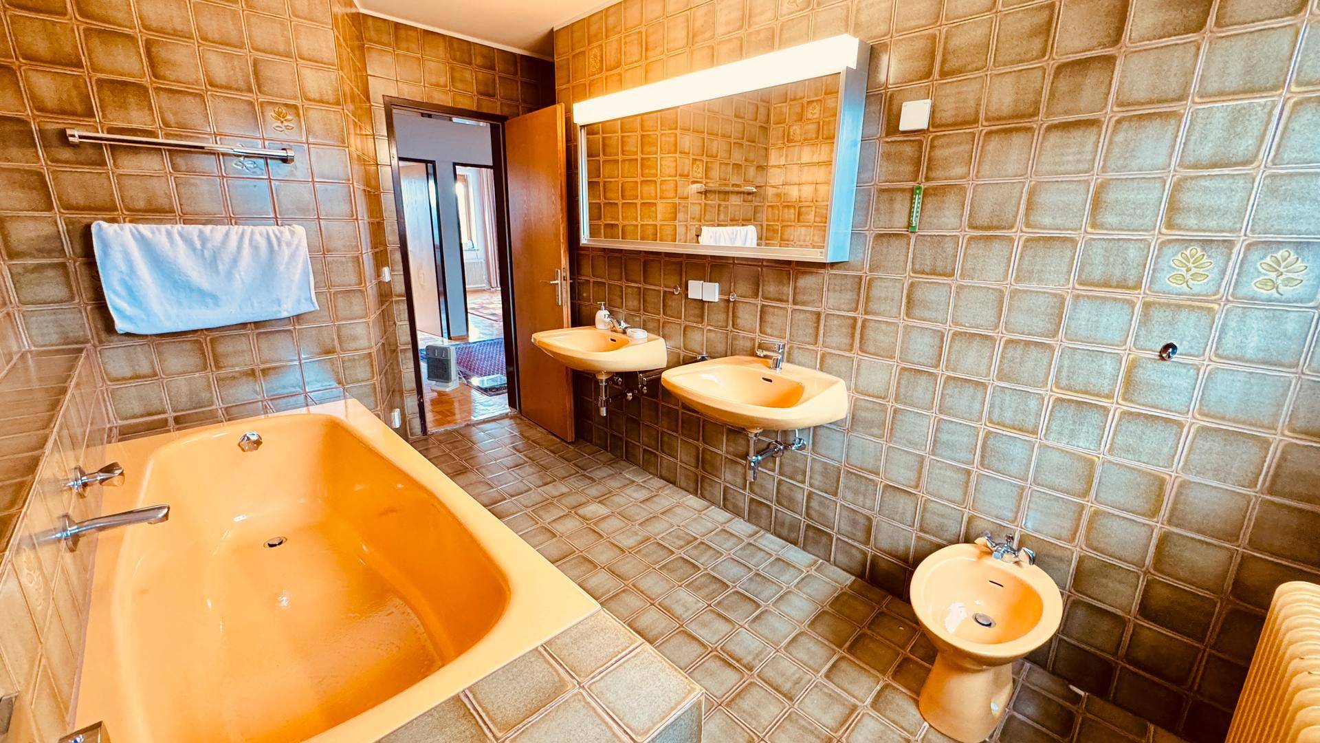 Badezimmer mit gelbem Bidet, Badewanne, Doppelwaschbecken und braunen Fliesen im 80er-Jahre-Stil.