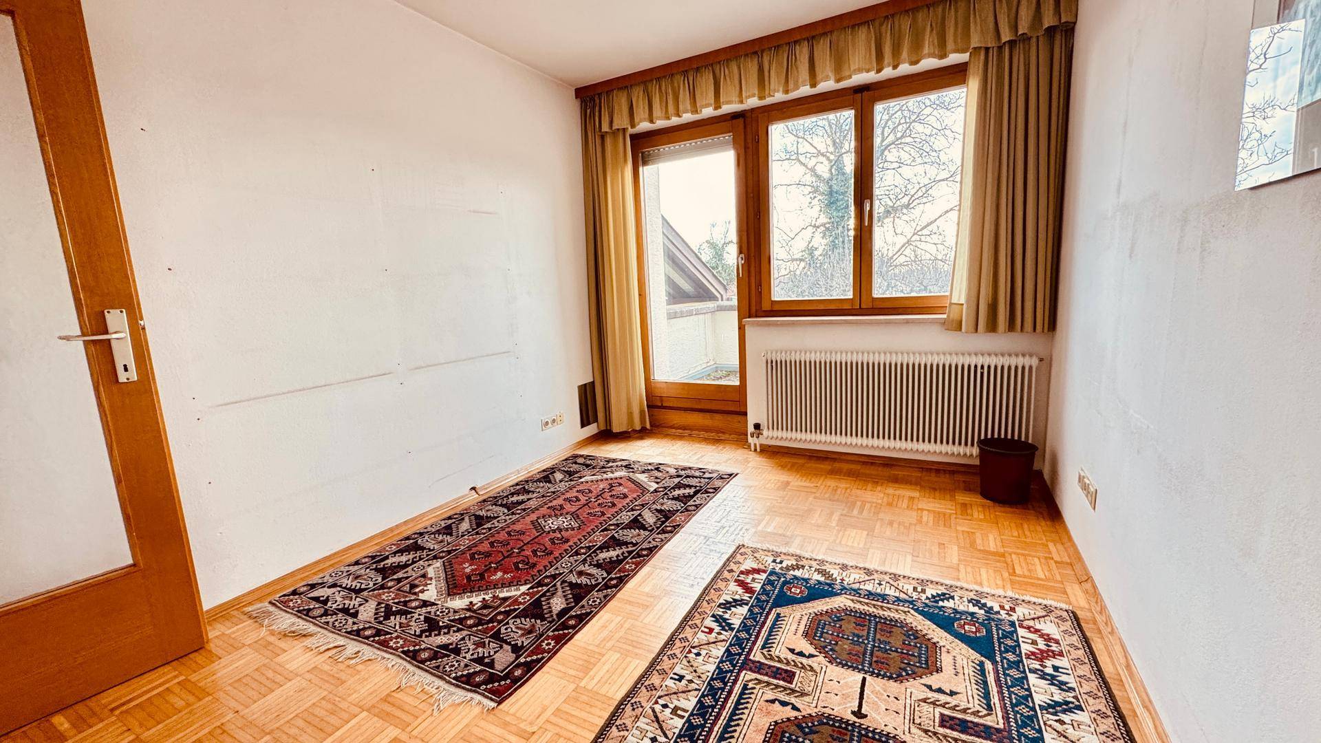 Helles Zimmer mit Parkettboden, großem Fenster und Heizkörper.