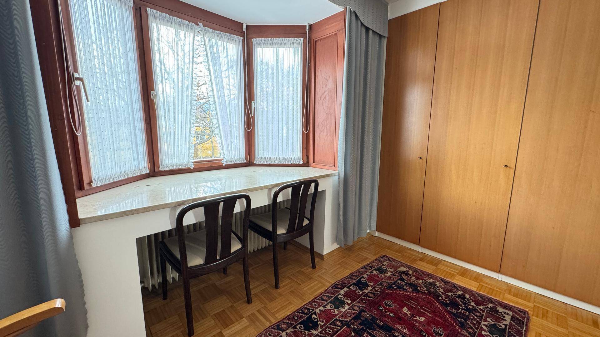 Zimmer mit Erkerfenster, integrierten Holzschränken und Parkettboden.