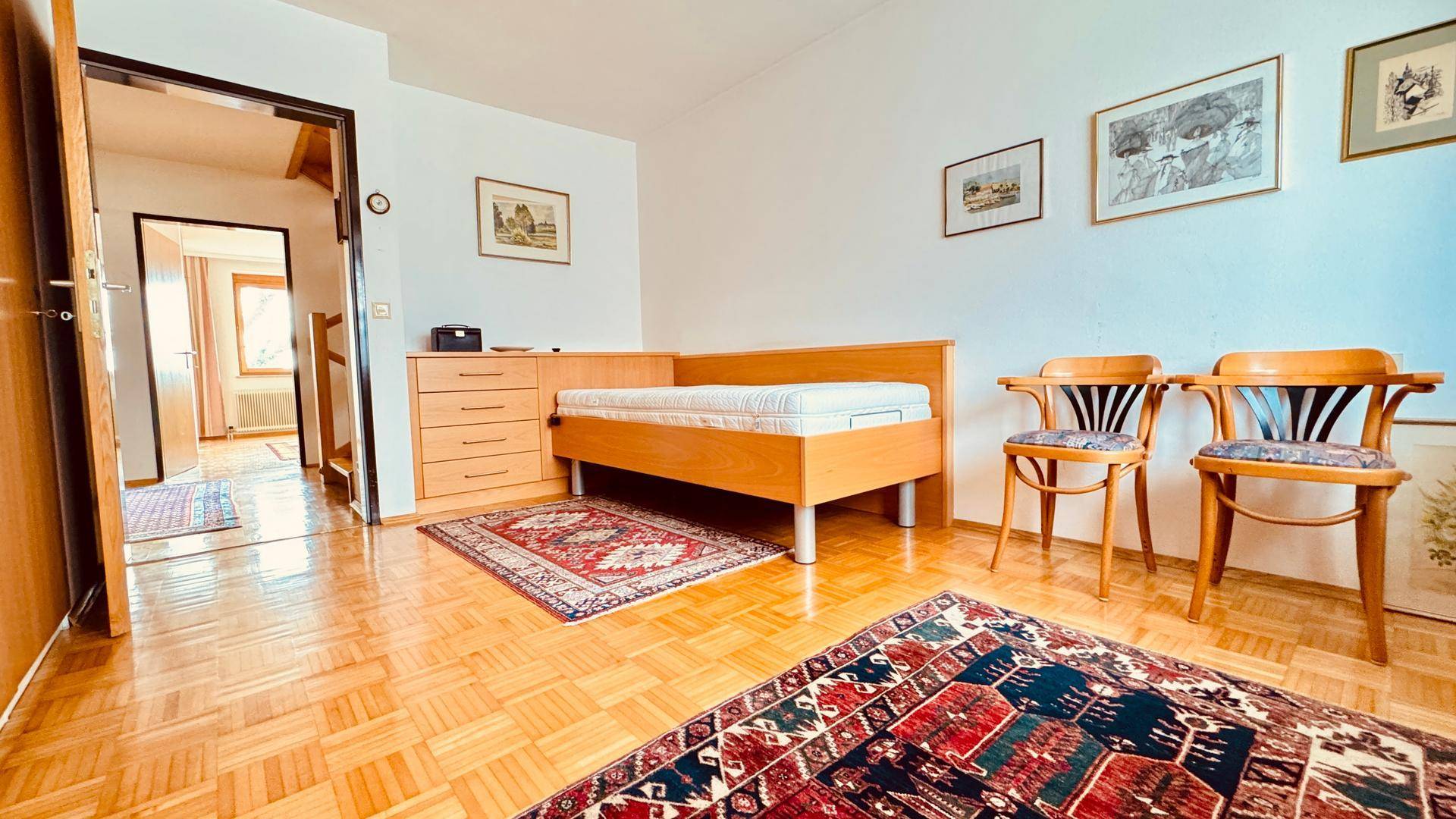 Schlafzimmer mit Einzelbett, Holzstühlen und Parkettboden.