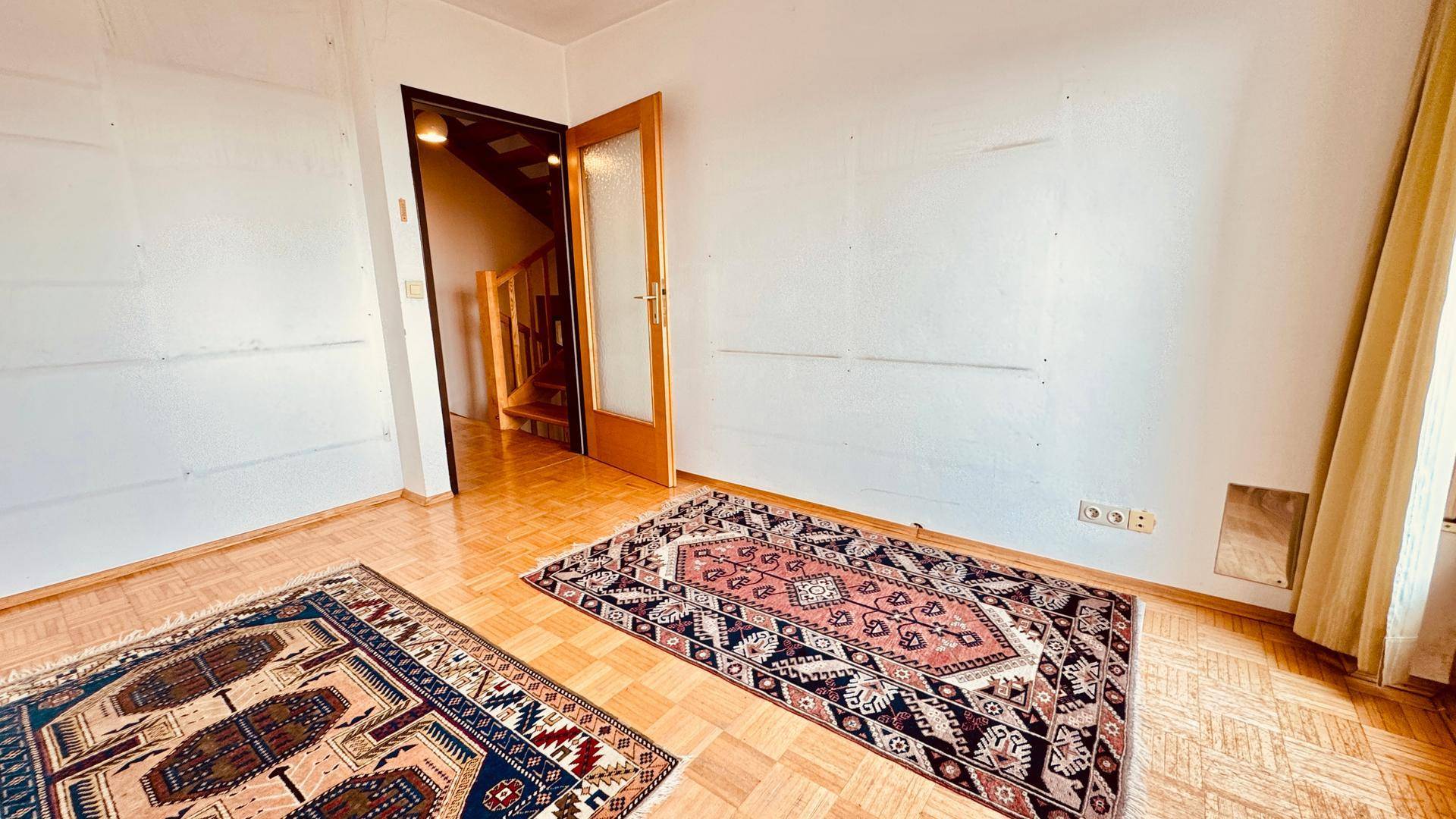 Leeres Zimmer mit Parkettboden und zwei Teppichen, bereit zur individuellen Gestaltung.