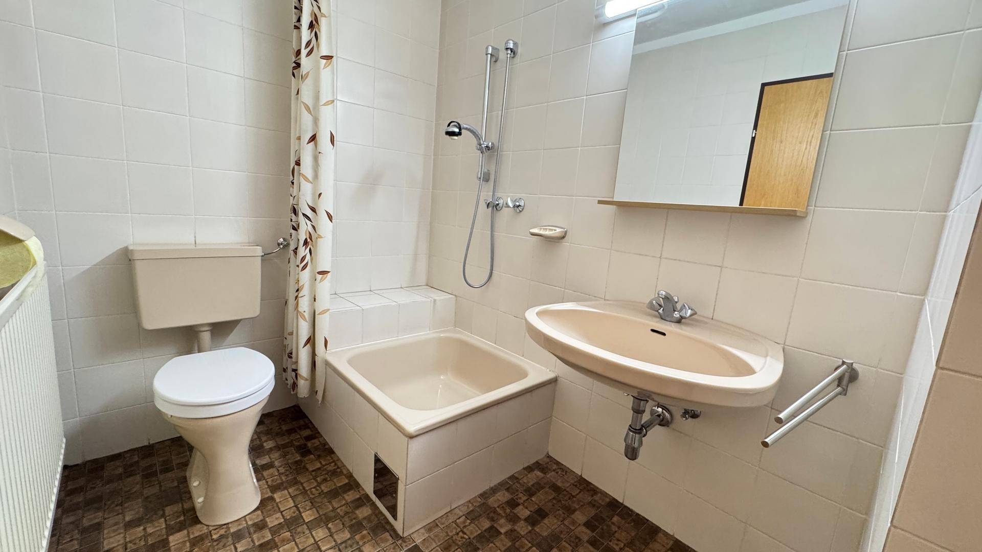 Badezimmer mit kleiner Badewanne, Duschvorrichtung und Einzelwaschbecken.