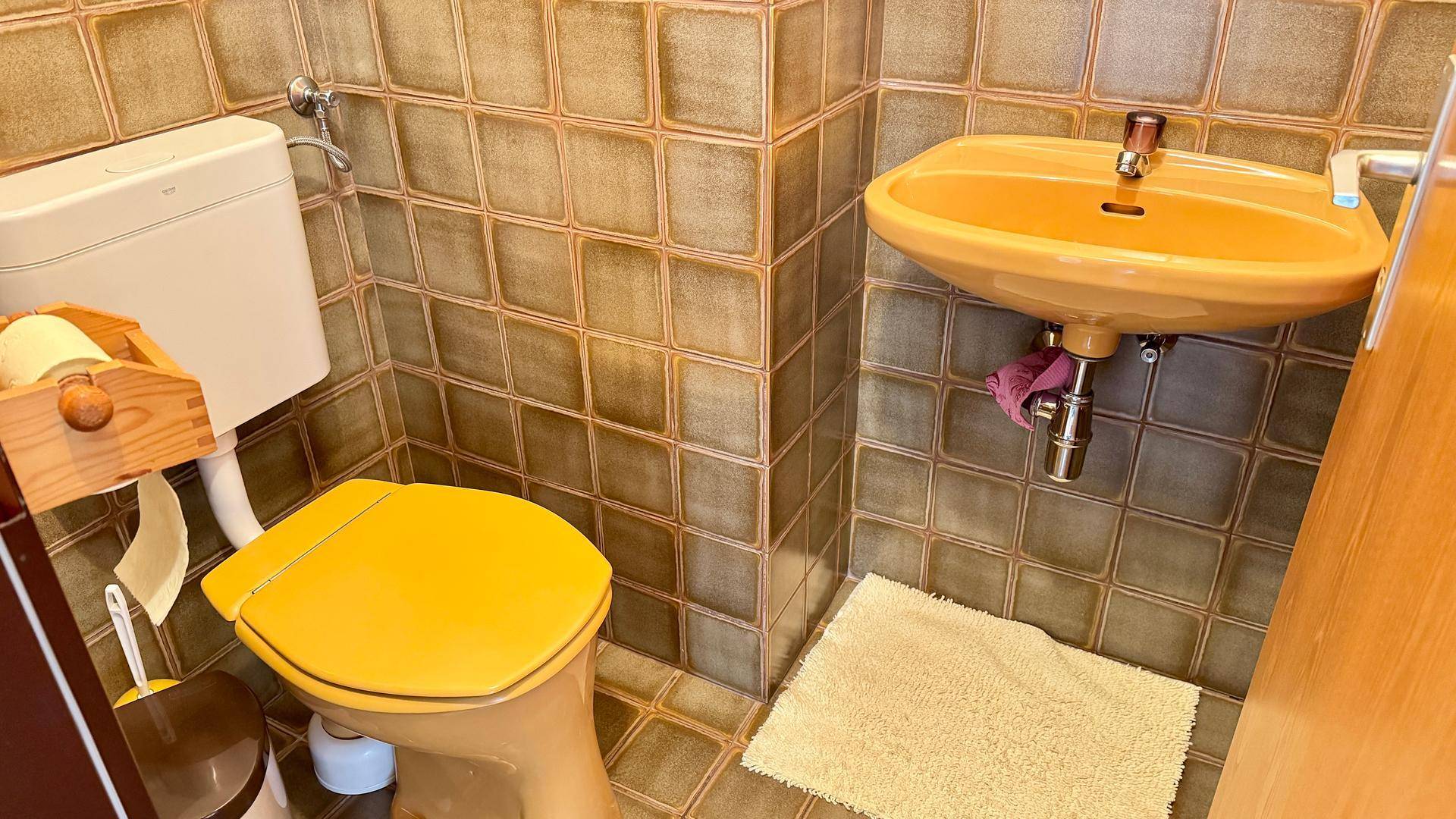 Gästetoilette mit gelben Sanitärobjekten und braunen Fliesen im 80er-Jahre-Stil.