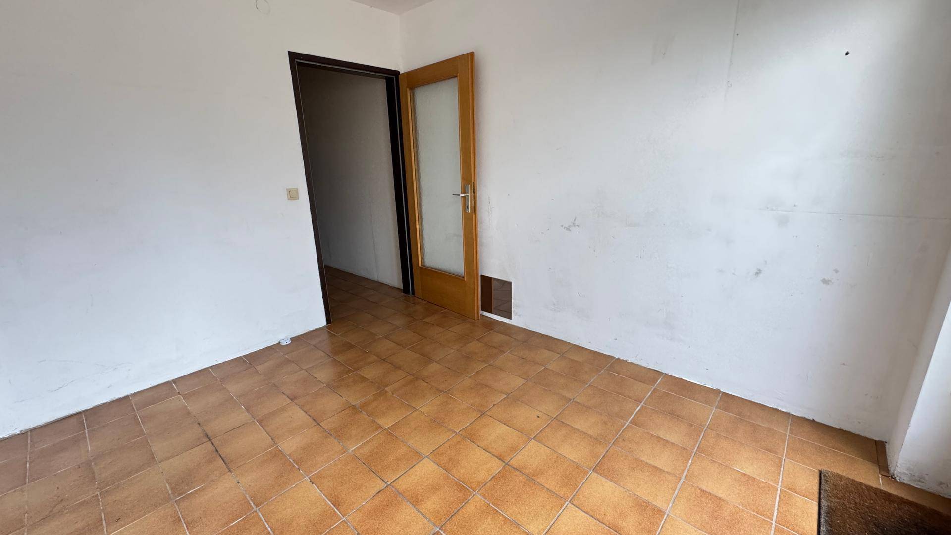 Leeres Zimmer mit Terrakottafliesen und weiß gestrichenen Wänden.