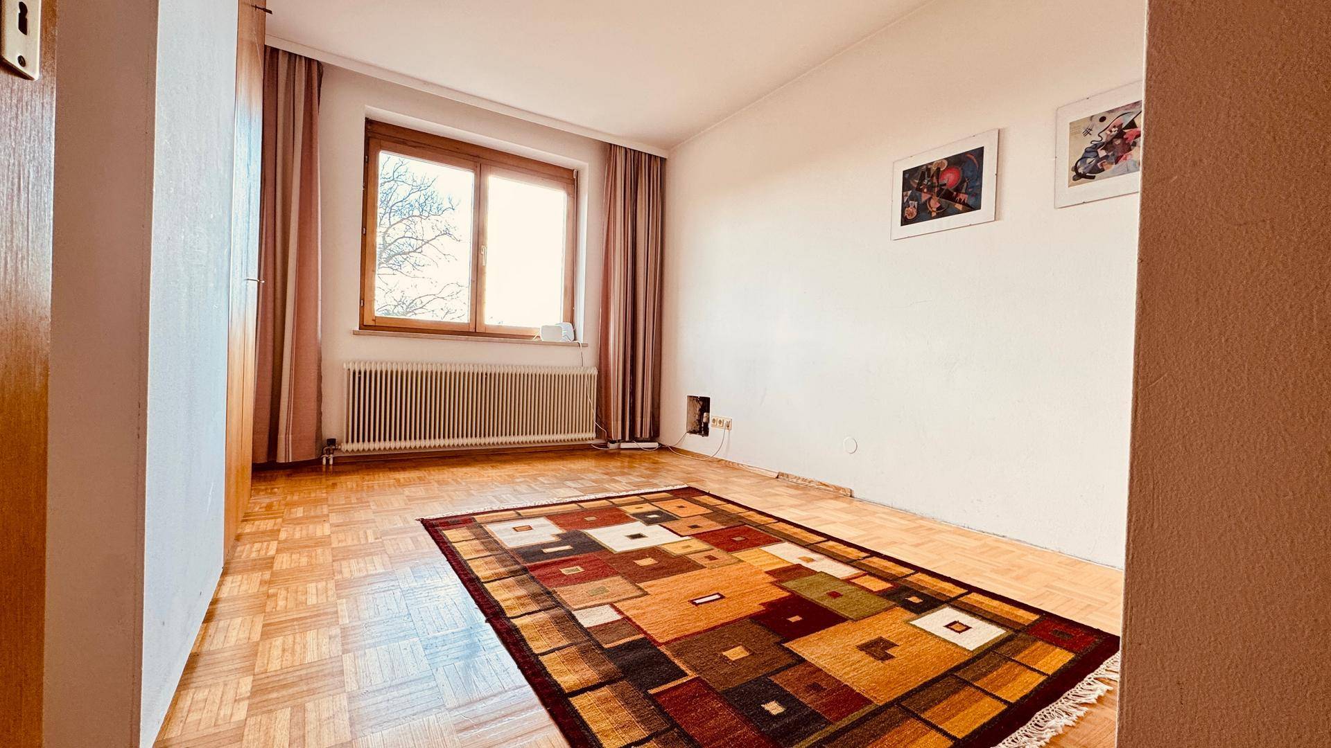 Leeres Zimmer mit Parkettboden und farbenfrohem Teppich.