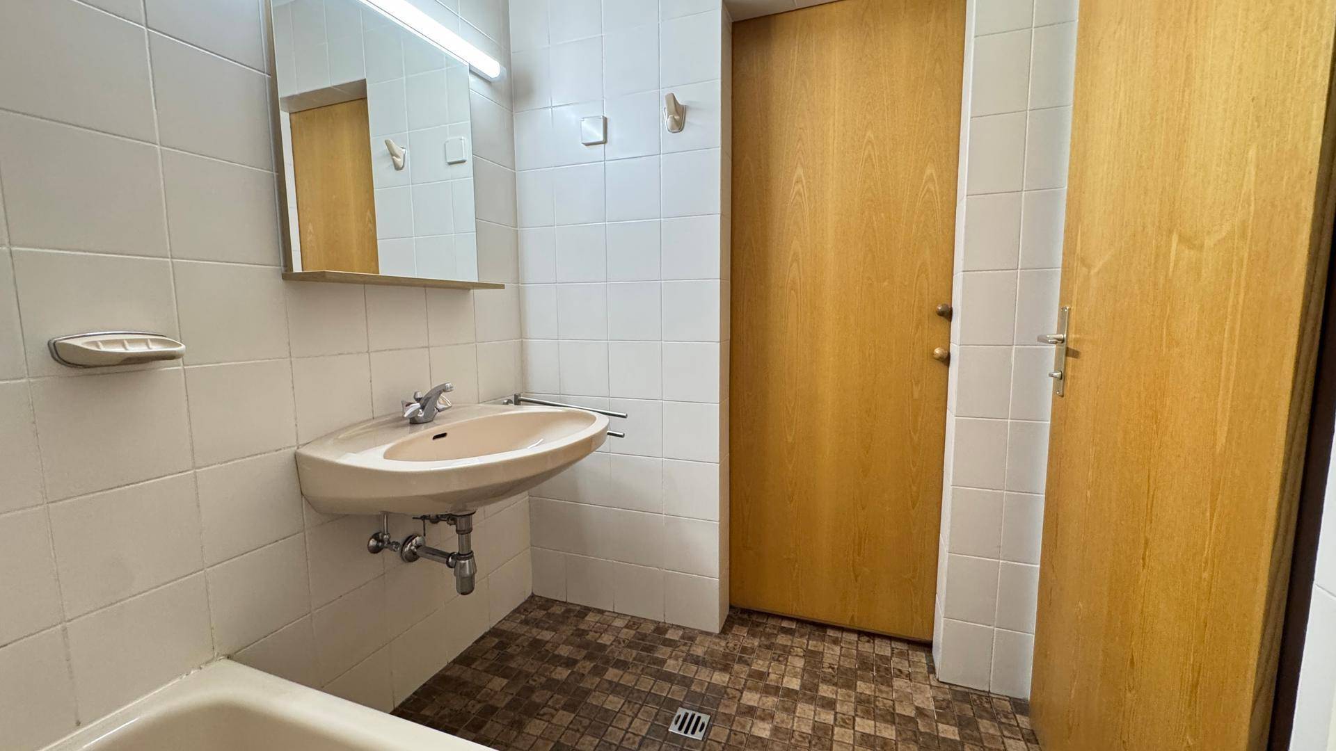 Badezimmer mit Einzelwaschbecken, Spiegelschrank und weißen Fliesen.