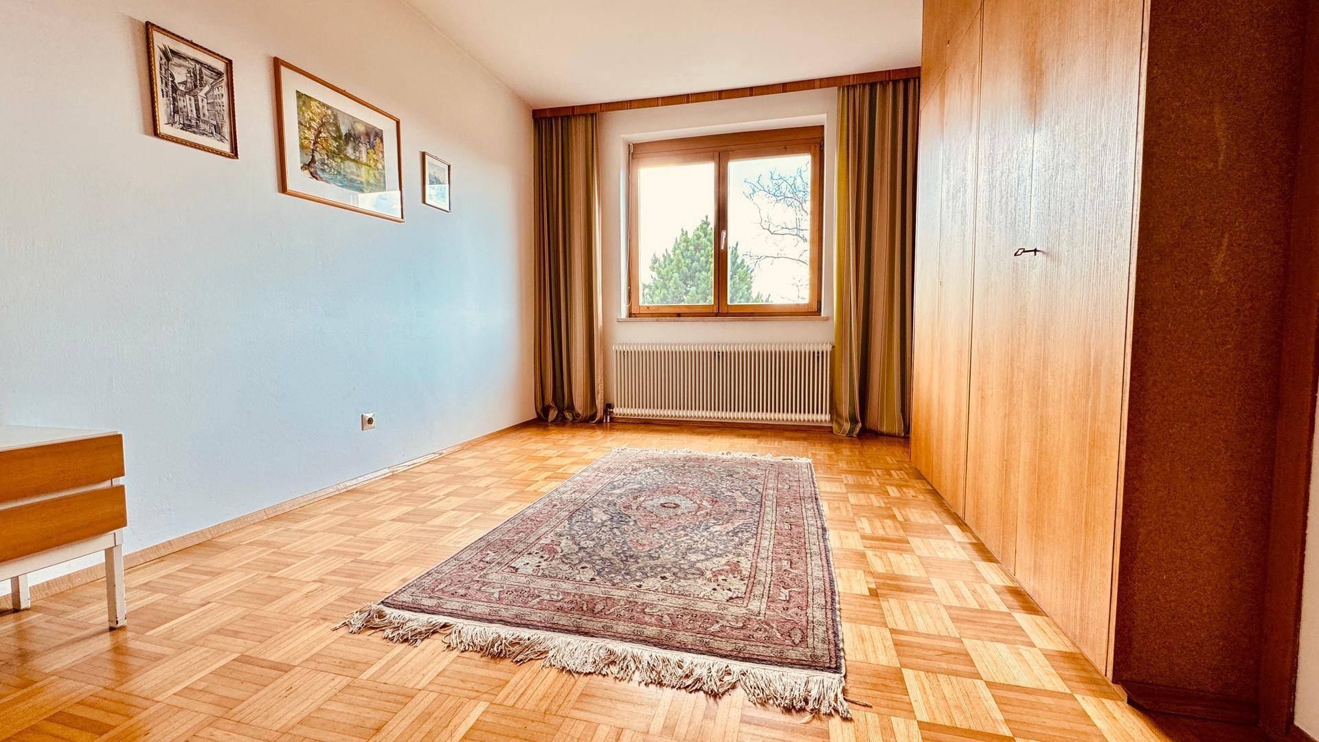 Schlafzimmer mit Einbauschrank, Parkettboden und Fenster.
