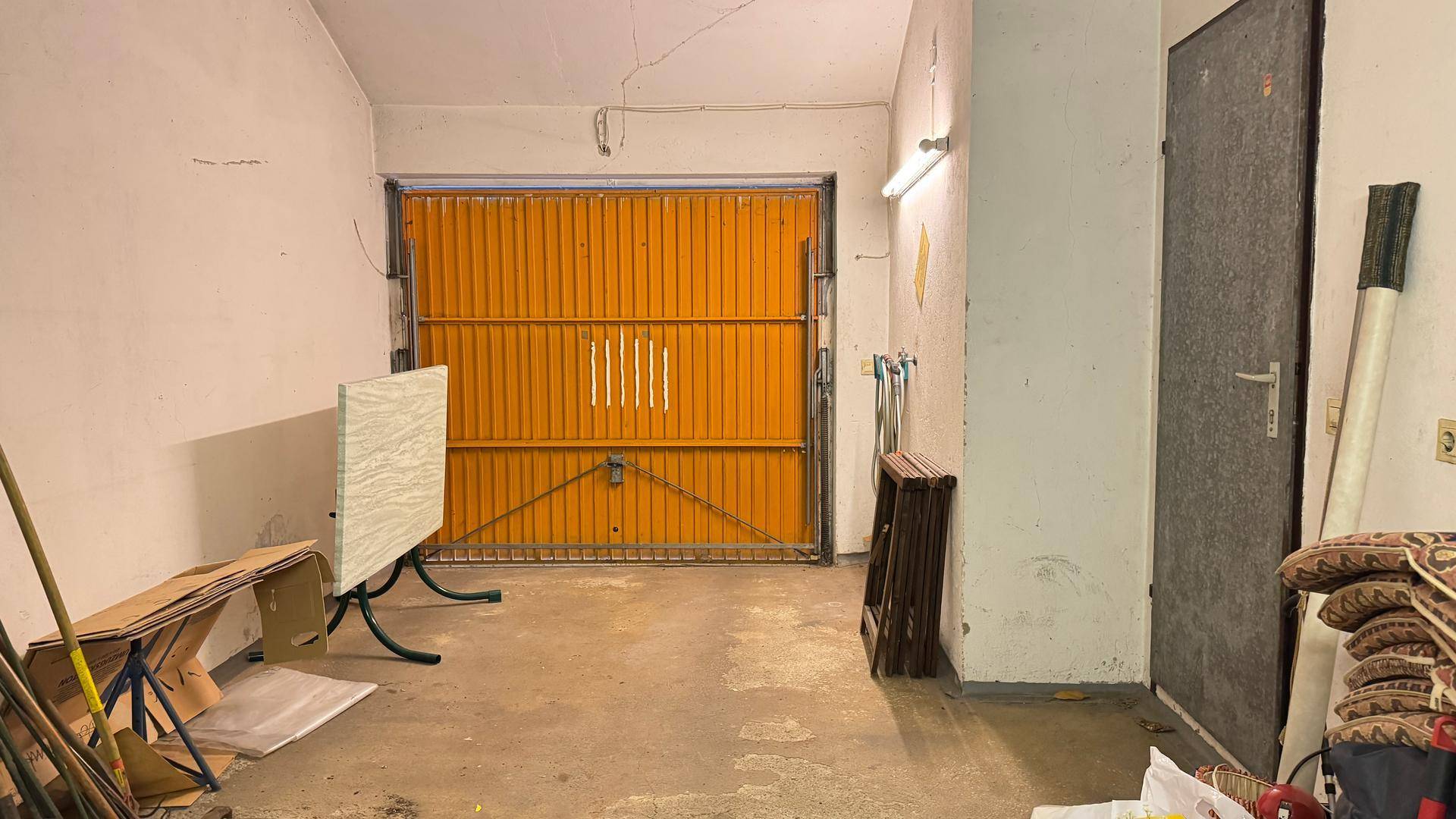 Geräumige Garage mit orangefarbenem Tor und Abstellmöglichkeiten.