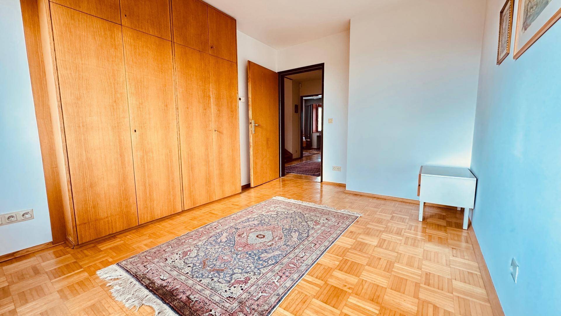 Leeres Zimmer mit Einbauschrank, Parkettboden und blauer Wand.