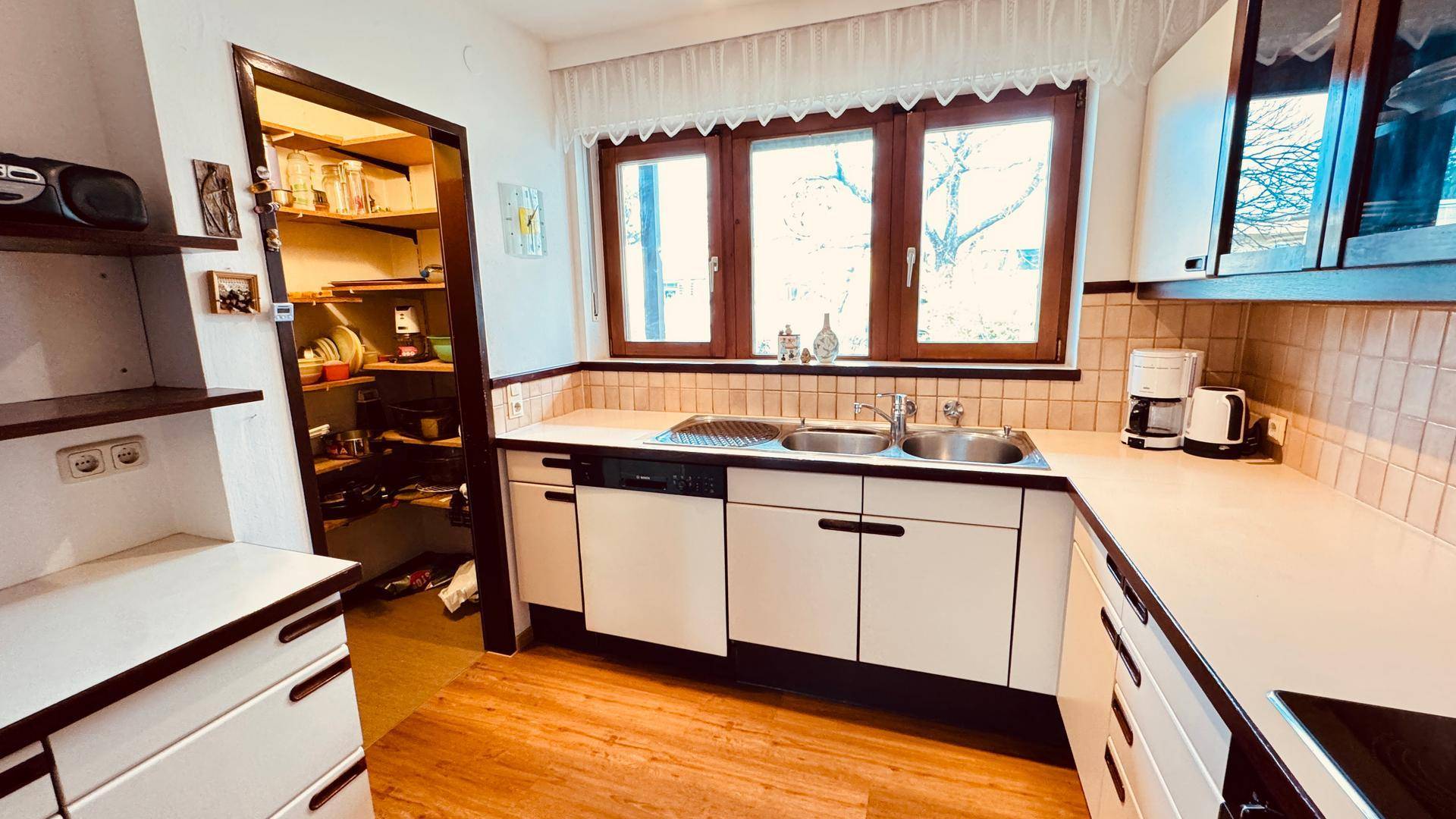 Funktionale Küche mit Fenster, Doppelspüle und Zugang zu einer Speisekammer.