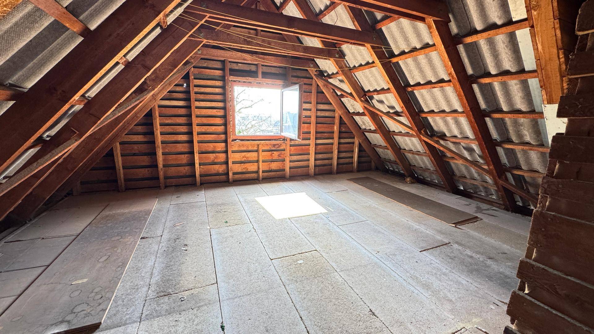 Ungenutzter Dachboden mit sichtbaren Holzbalken und Fenster.
