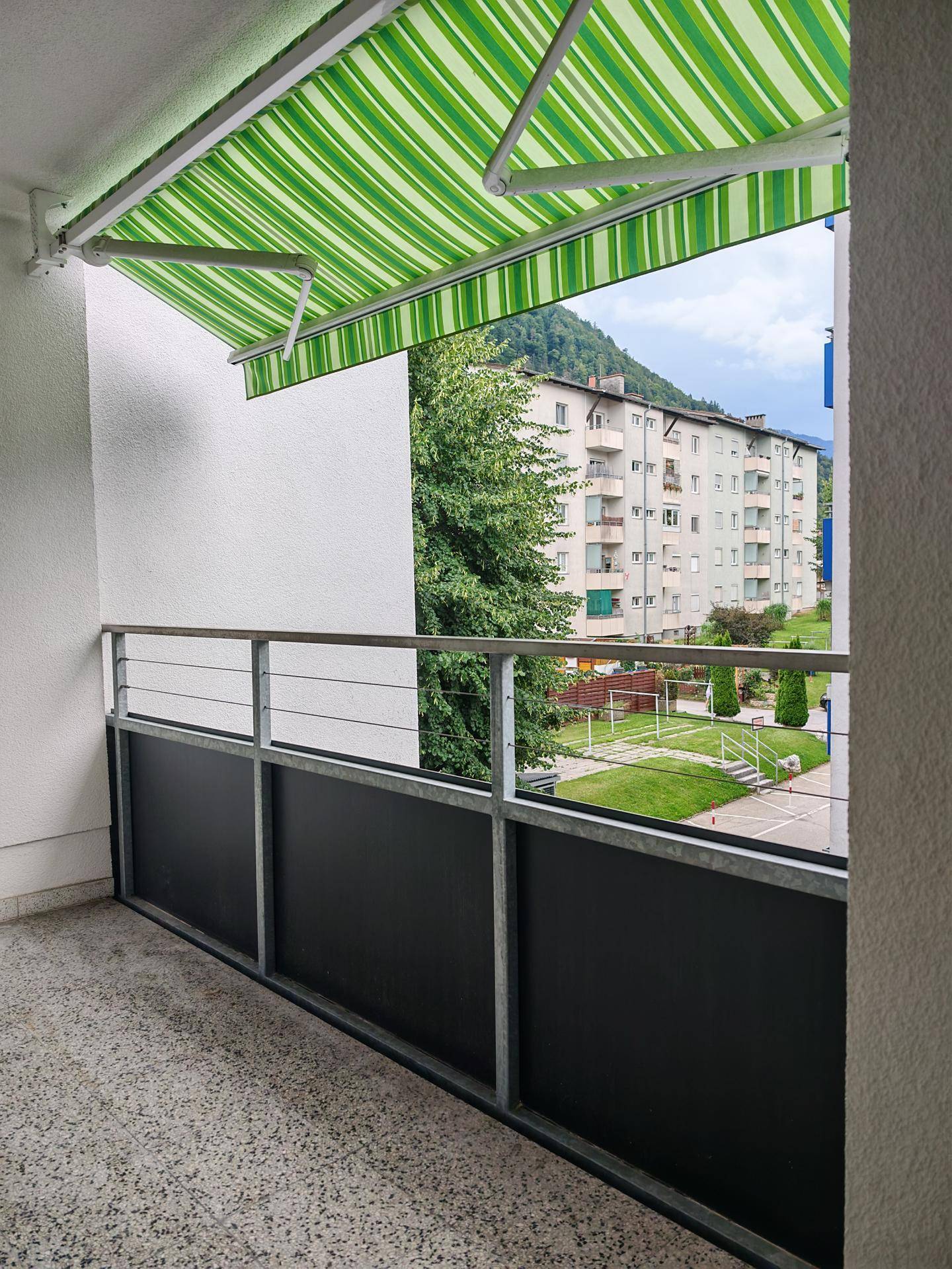 Balkon mit gestreifter Markise und Blick auf die umliegenden Gebäude und Grünflächen.