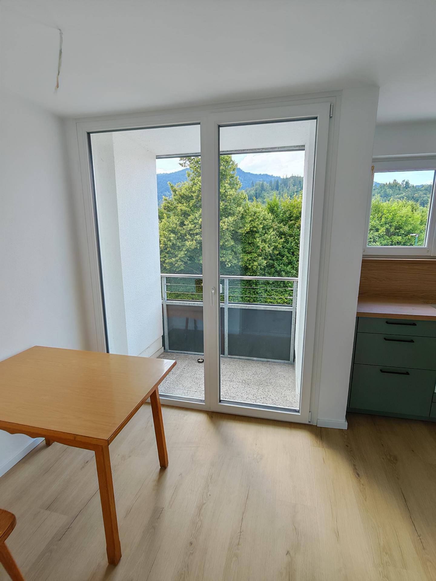 Heller Essbereich mit Holztisch und großem Fenster mit Zugang zum Balkon und Bergblick.
