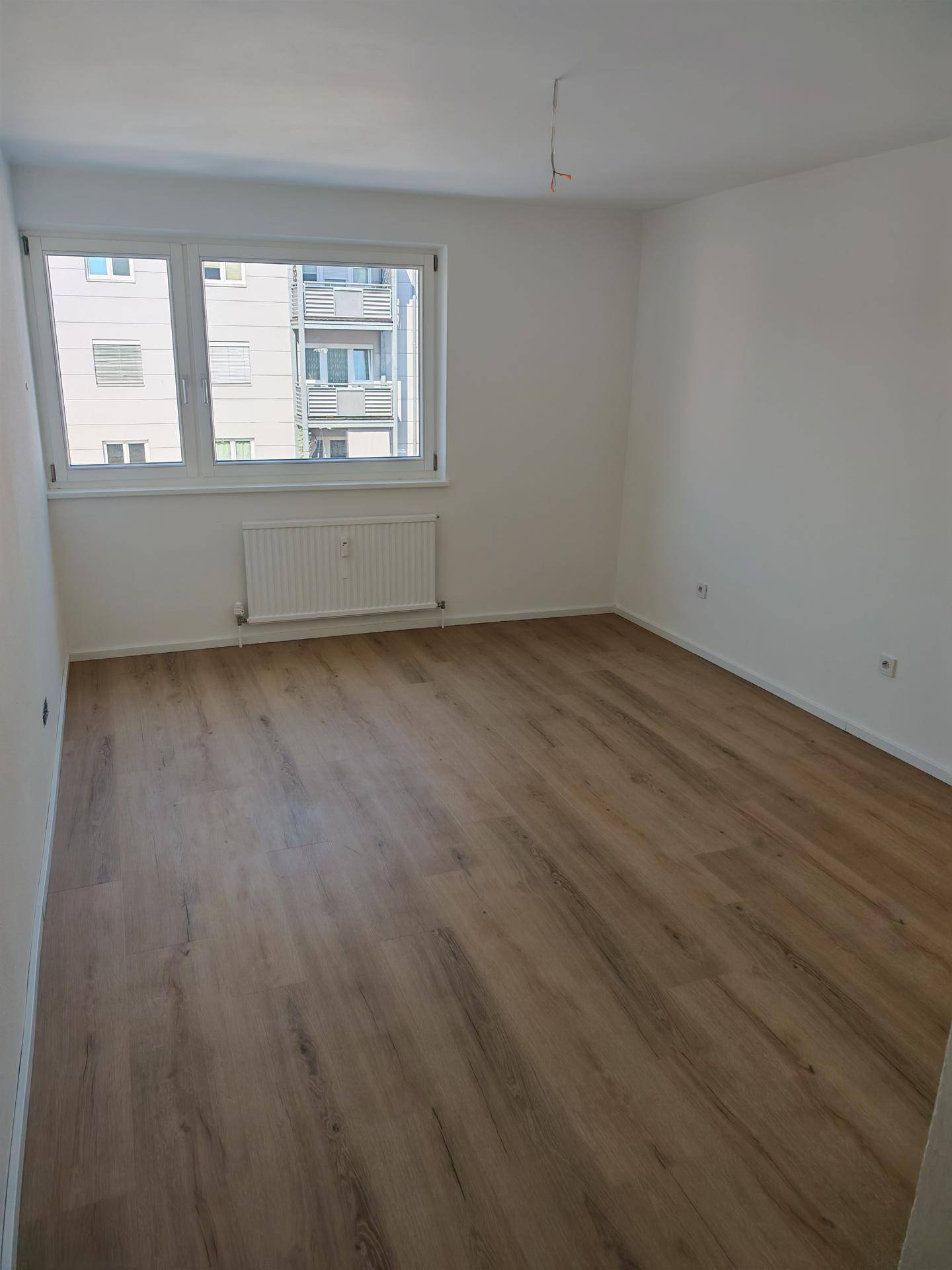 Leeres Zimmer mit hellem Laminatboden und Fenster mit Blick auf die städtische Umgebung.