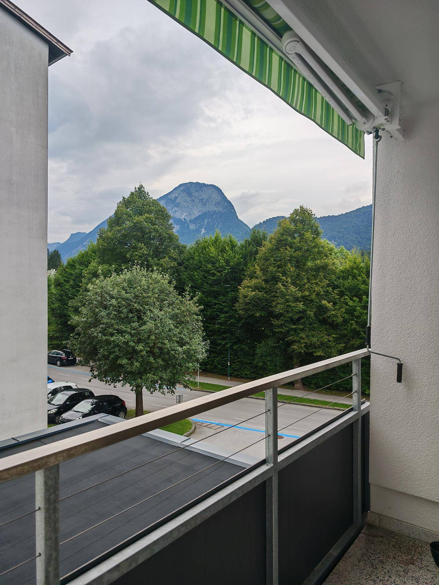 Balkon mit gestreifter Markise und weitem Blick auf Berge und grüne Umgebung.