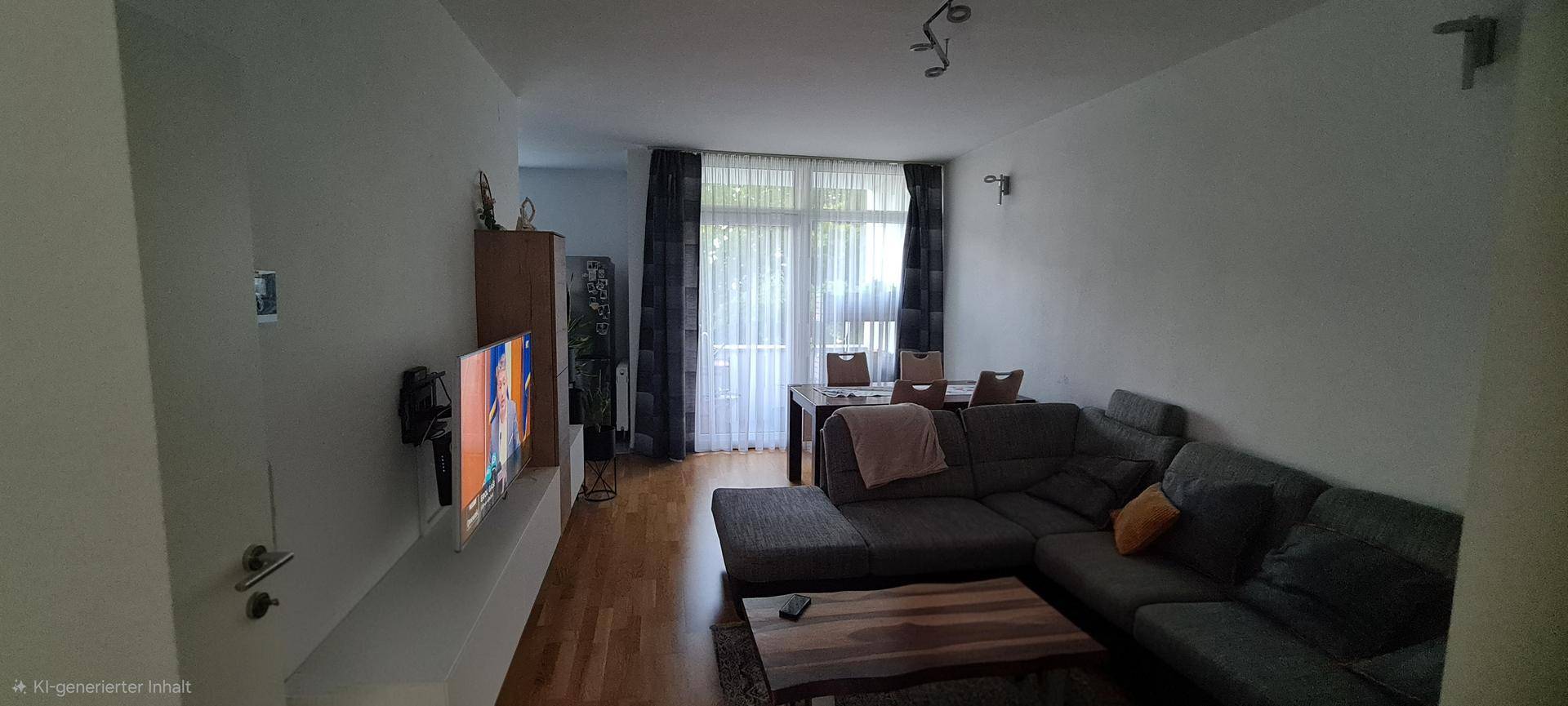 Gemütlicher Wohn-Essbereich mit großem Sofa, Fernseher und Zugang zum Balkon.