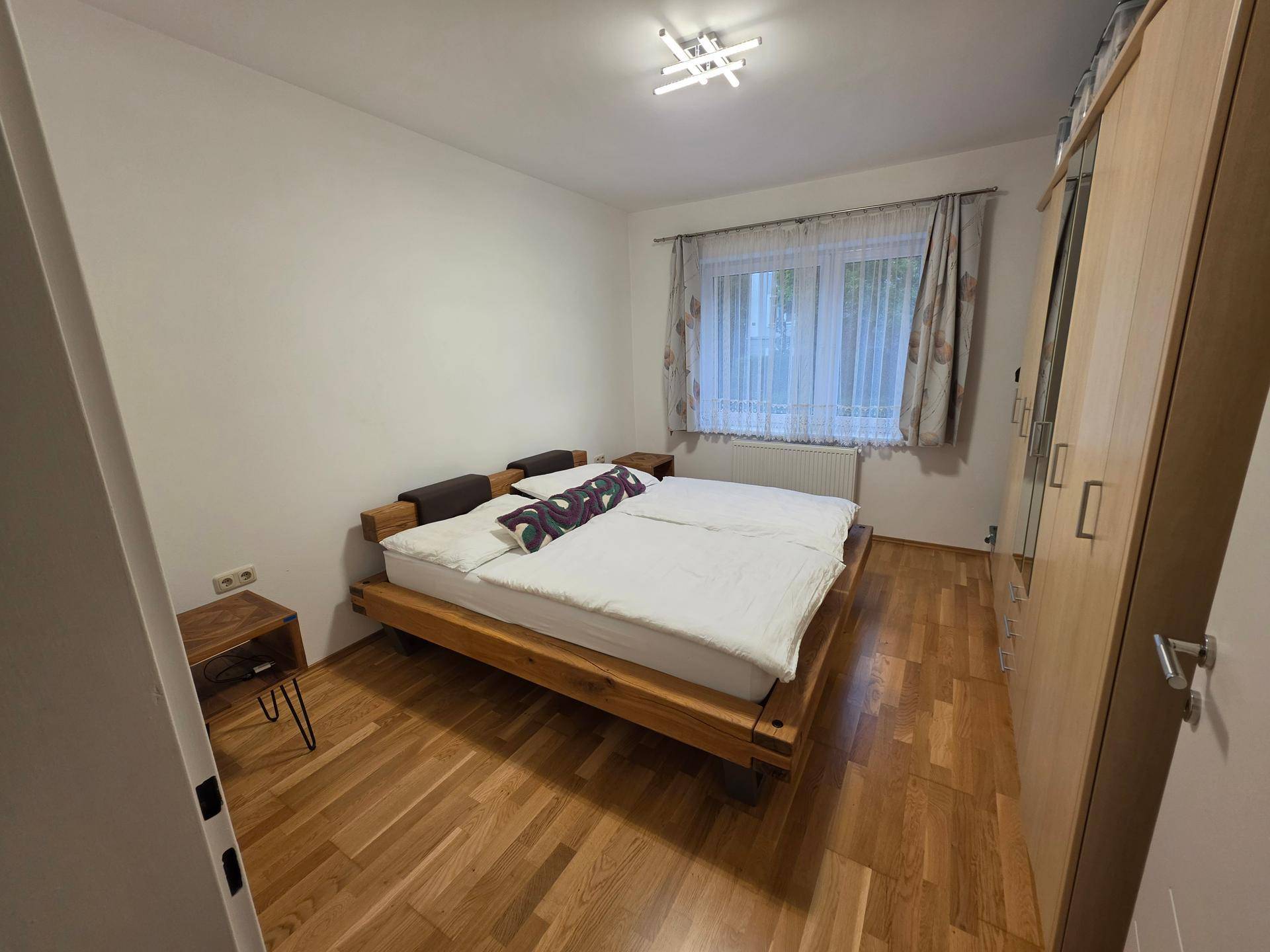 Schlafzimmer mit Holzbett, Kleiderschrank und Parkettboden.