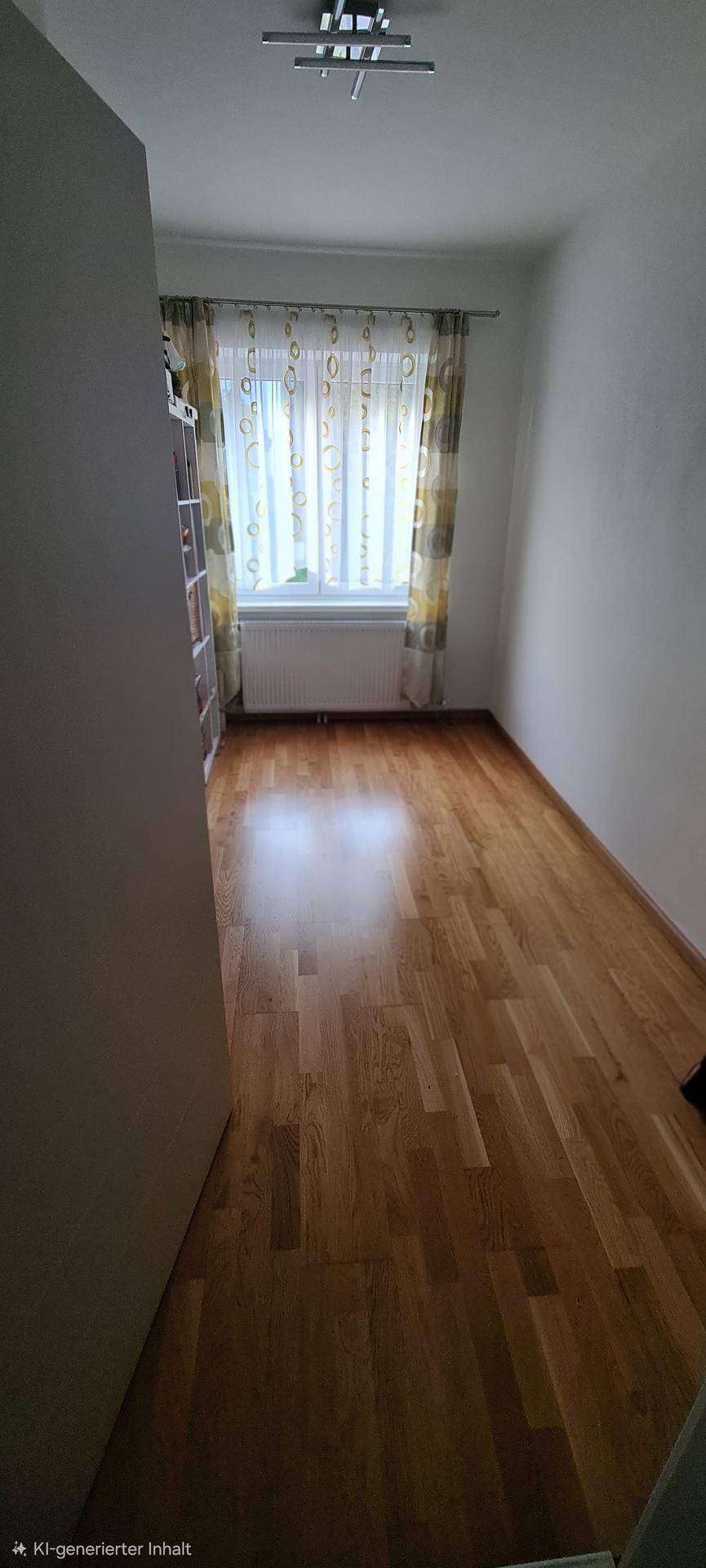 Leeres Zimmer mit Parkettboden und einem Fenster mit Vorhängen.