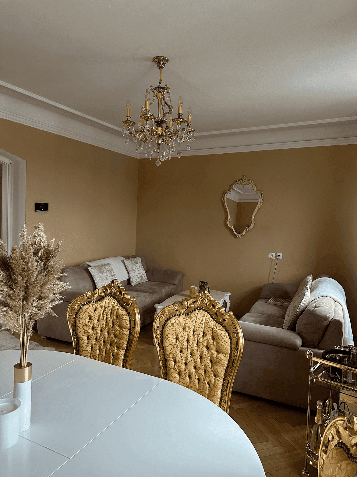 Geräumiger Wohn-Essbereich mit Kronleuchter, beigen Sofas und eleganten goldenen Stühlen.
