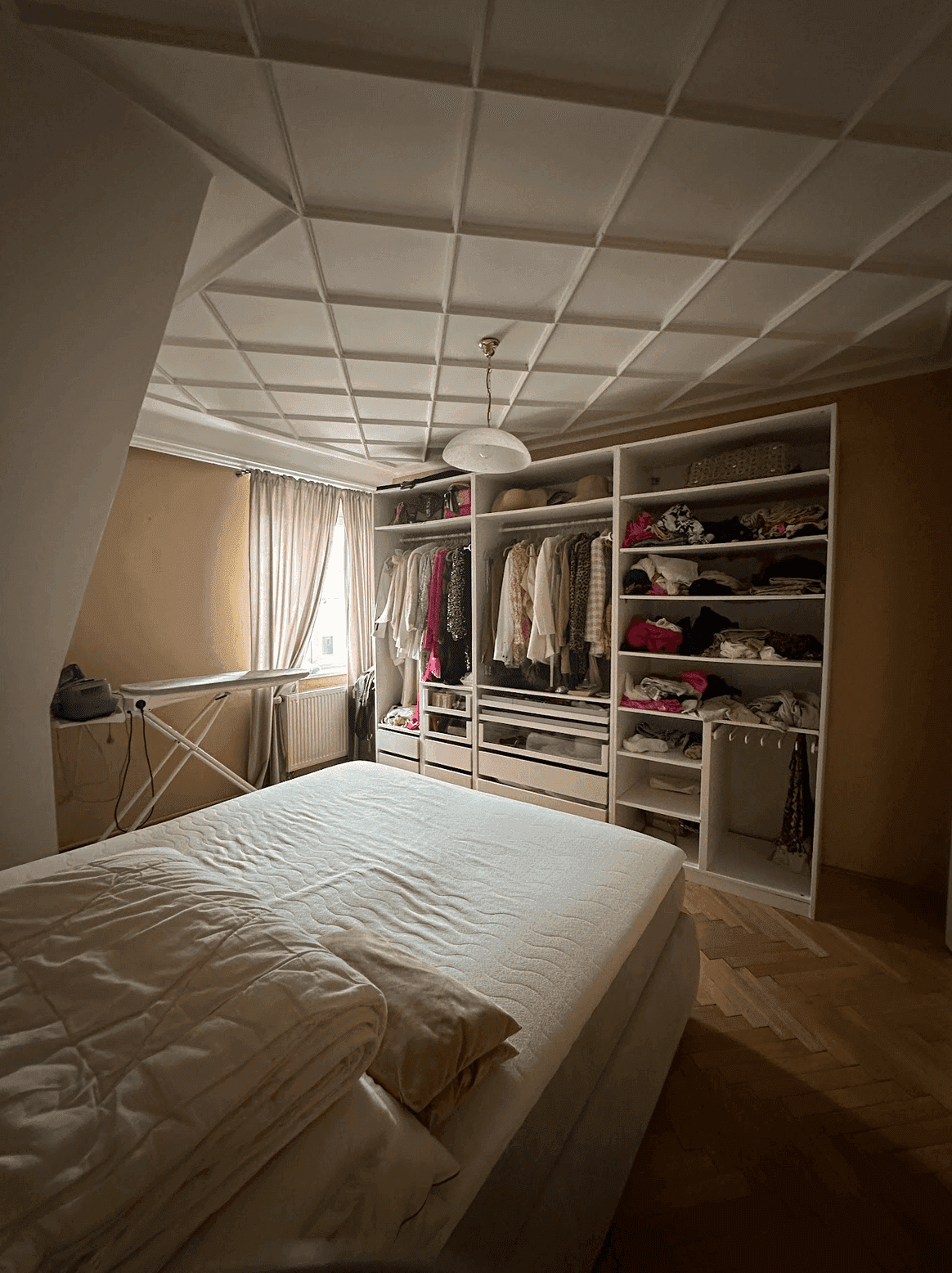 Schlafzimmer mit großem, integriertem Kleiderschrank, Fischgrätparkett und einer strukturierten Decke.