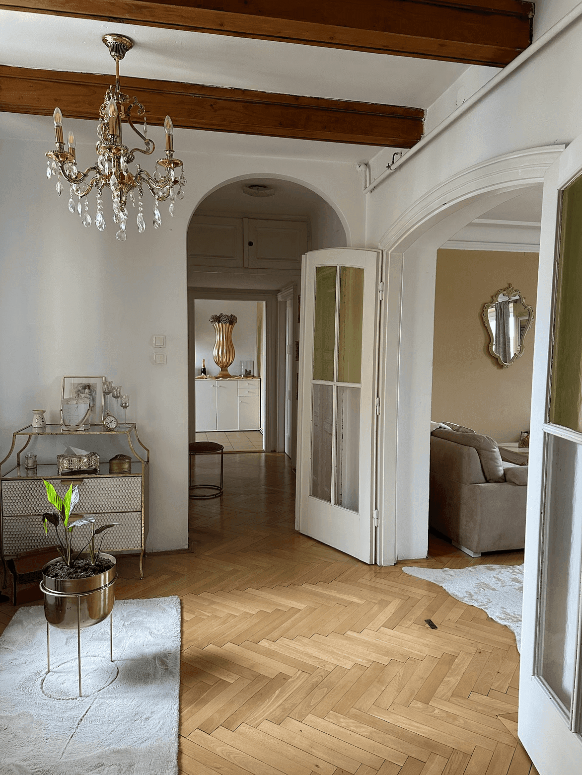Heller Flur mit Fischgrätparkett, sichtbaren Holzbalken und einem eleganten Kronleuchter, der in weitere Räume führt.
