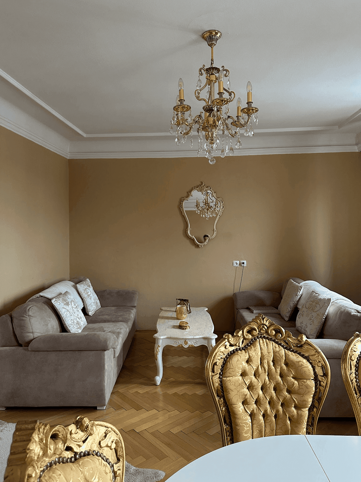 Geräumiger Wohn-Essbereich mit beigen Sofas, goldenen Stühlen und einem eleganten Kronleuchter.