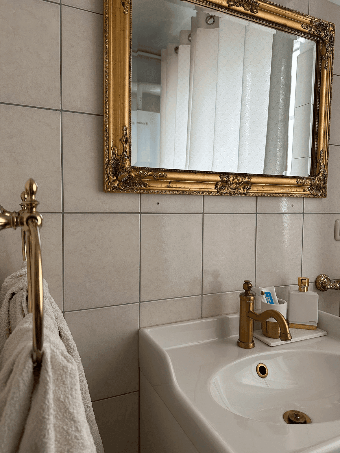 Badezimmer mit goldenen Armaturen, einem Waschbecken und einem opulenten Spiegel über den Fliesen.