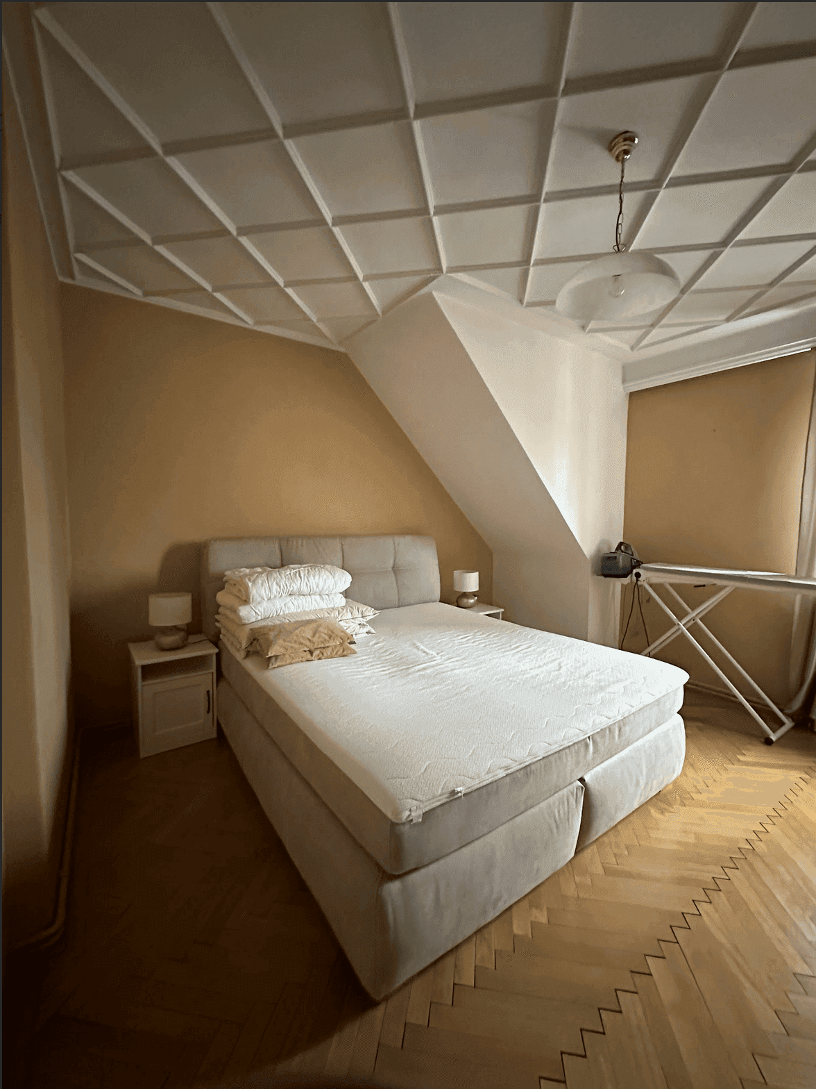 Gemütliches Schlafzimmer mit Boxspringbett, Fischgrätparkett und einer dekorativen Deckenstruktur.