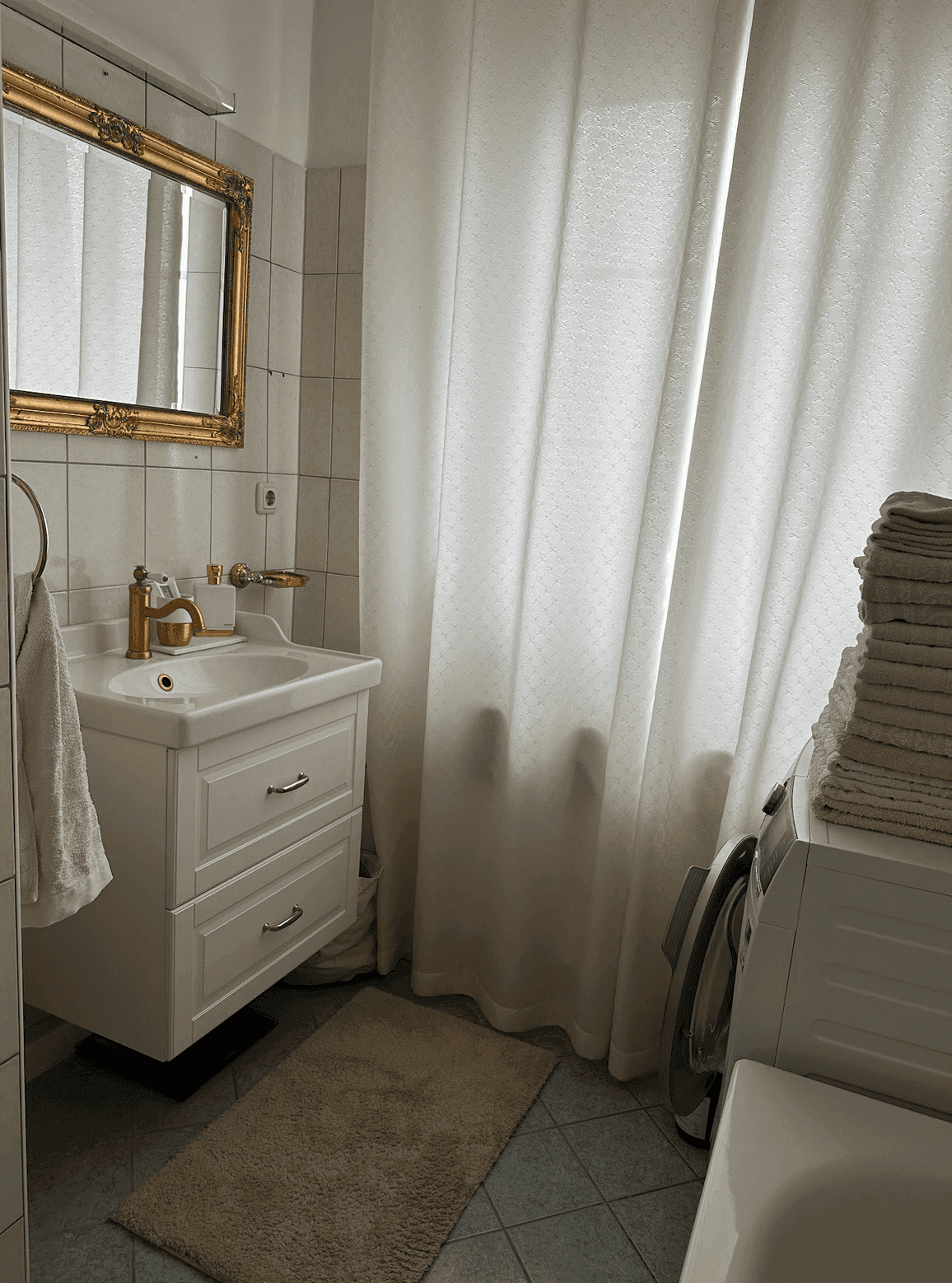 Helles Badezimmer mit Waschbecken, Waschmaschine und einer Badewanne hinter dem Duschvorhang.