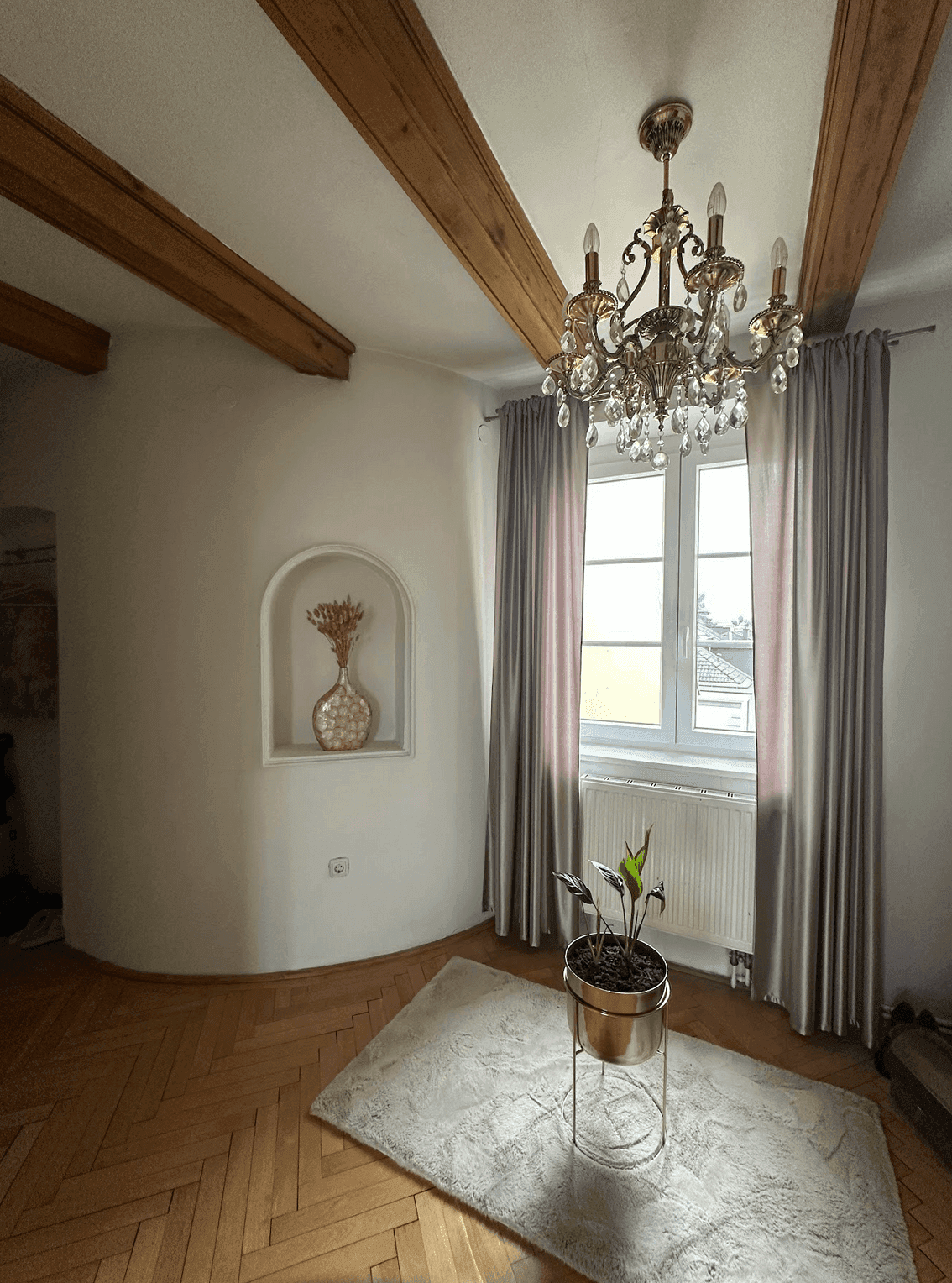 Elegantes Zimmer mit sichtbaren Holzbalken, einem prunkvollen Kronleuchter und Fischgrätparkett.
