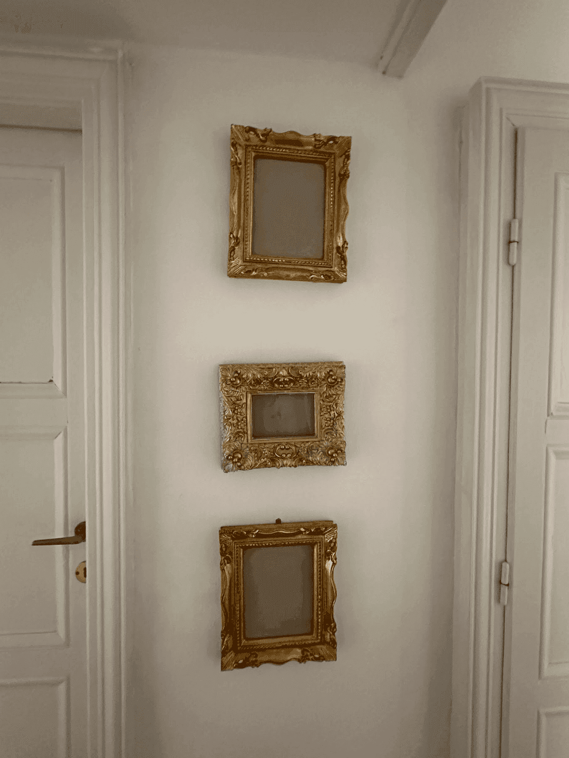 Detailaufnahme von drei leeren, goldgerahmten Bildern an einer weißen Wand im Flur.