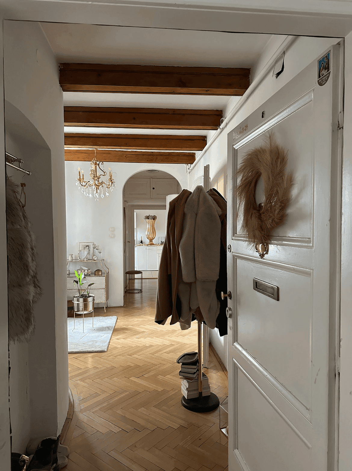 Eingangsbereich mit Garderobe, Fischgrätparkett und sichtbaren Holzbalken, der in weitere Räume führt.