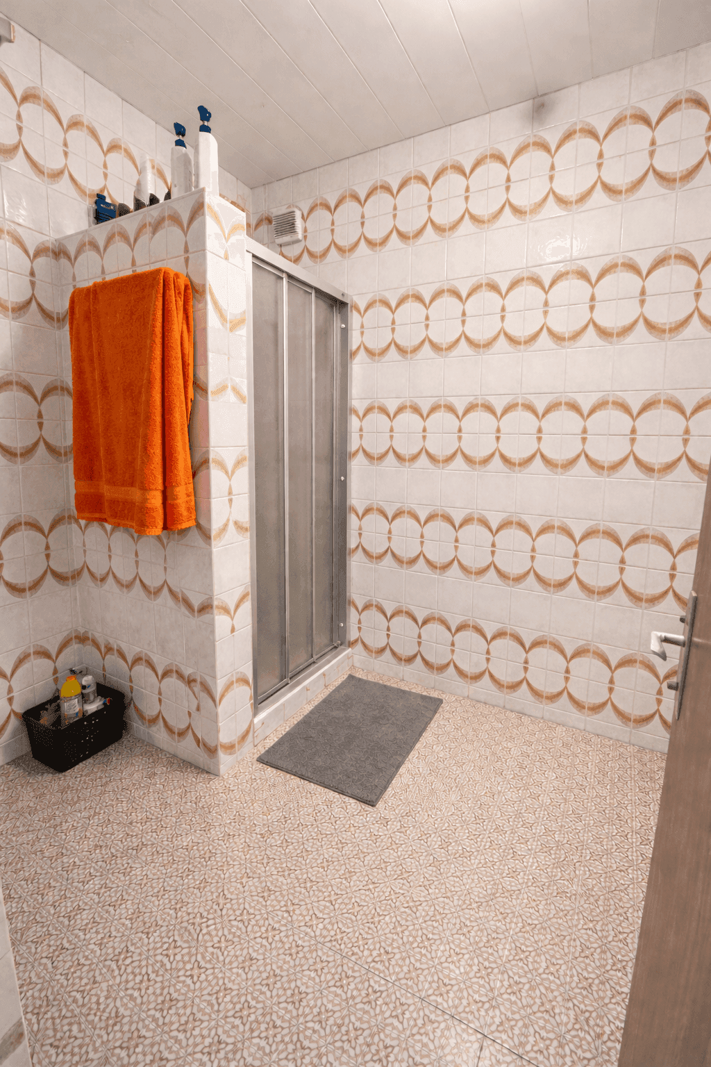 Badezimmer mit auffälligen orange-weißen Fliesen, einer Duschkabine und einem orangefarbenen Handtuch.