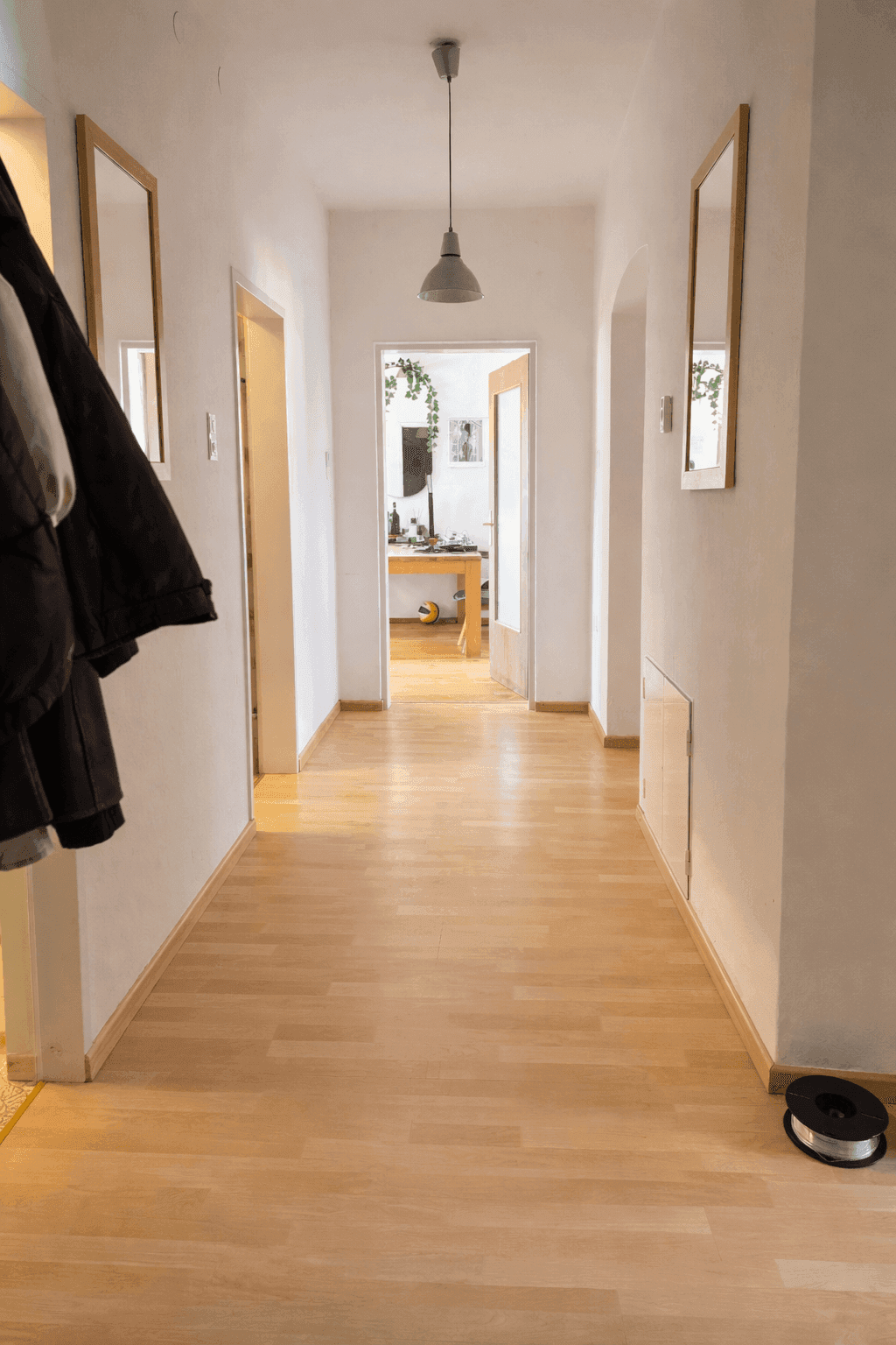 Heller Flur mit Holzfußboden, weißen Wänden und Spiegeln, der zu weiteren Räumen führt.