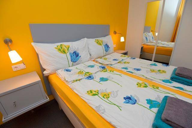 Helles Schlafzimmer mit zwei Einzelbetten, gelber Wand und floraler Bettwäsche.