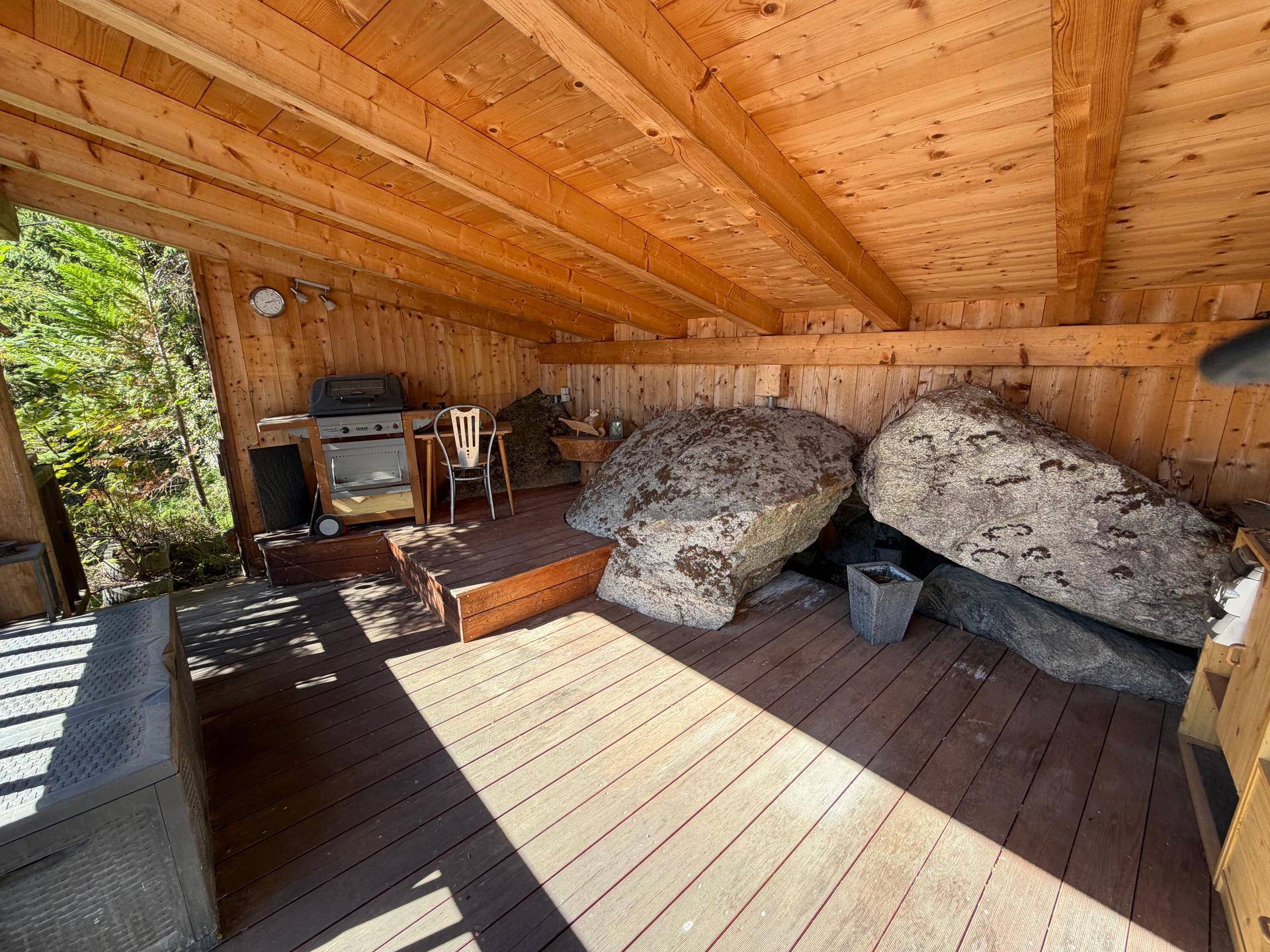 Rustikale Holzterrasse mit integrierten Felsen und überdachtem Grillbereich.