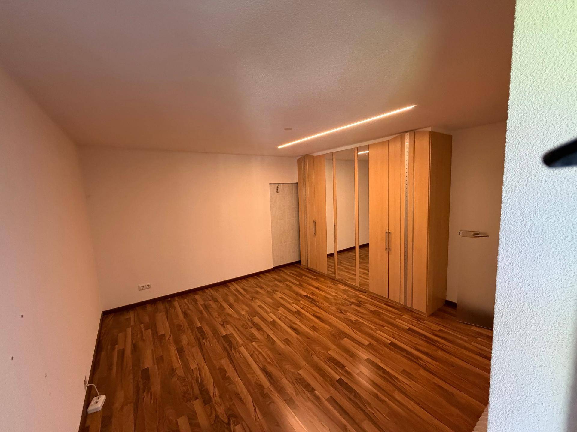 Helles Schlafzimmer mit Holzboden und großem Einbauschrank mit Spiegeltüren.