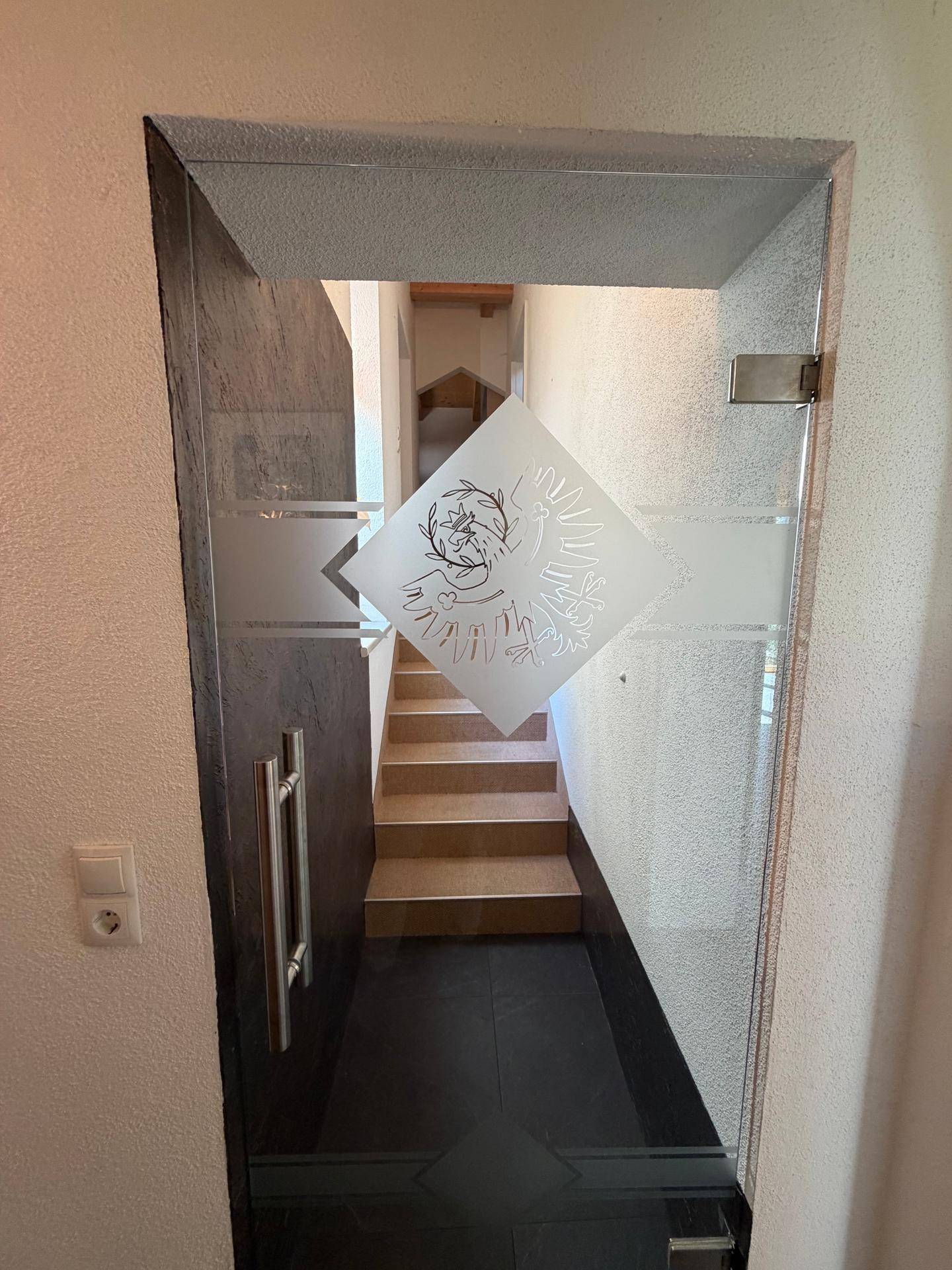 Eingangsbereich mit moderner Glastür und Blick auf die Treppe zum oberen Stockwerk.