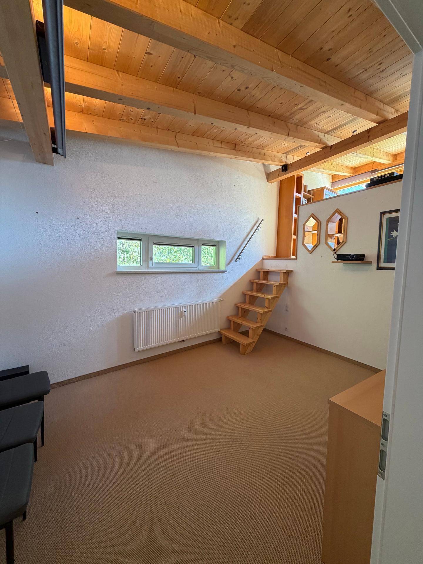 Geräumiger Wohnbereich mit Holzbalkendecke, Teppichboden und Treppe zum oberen Geschoss.