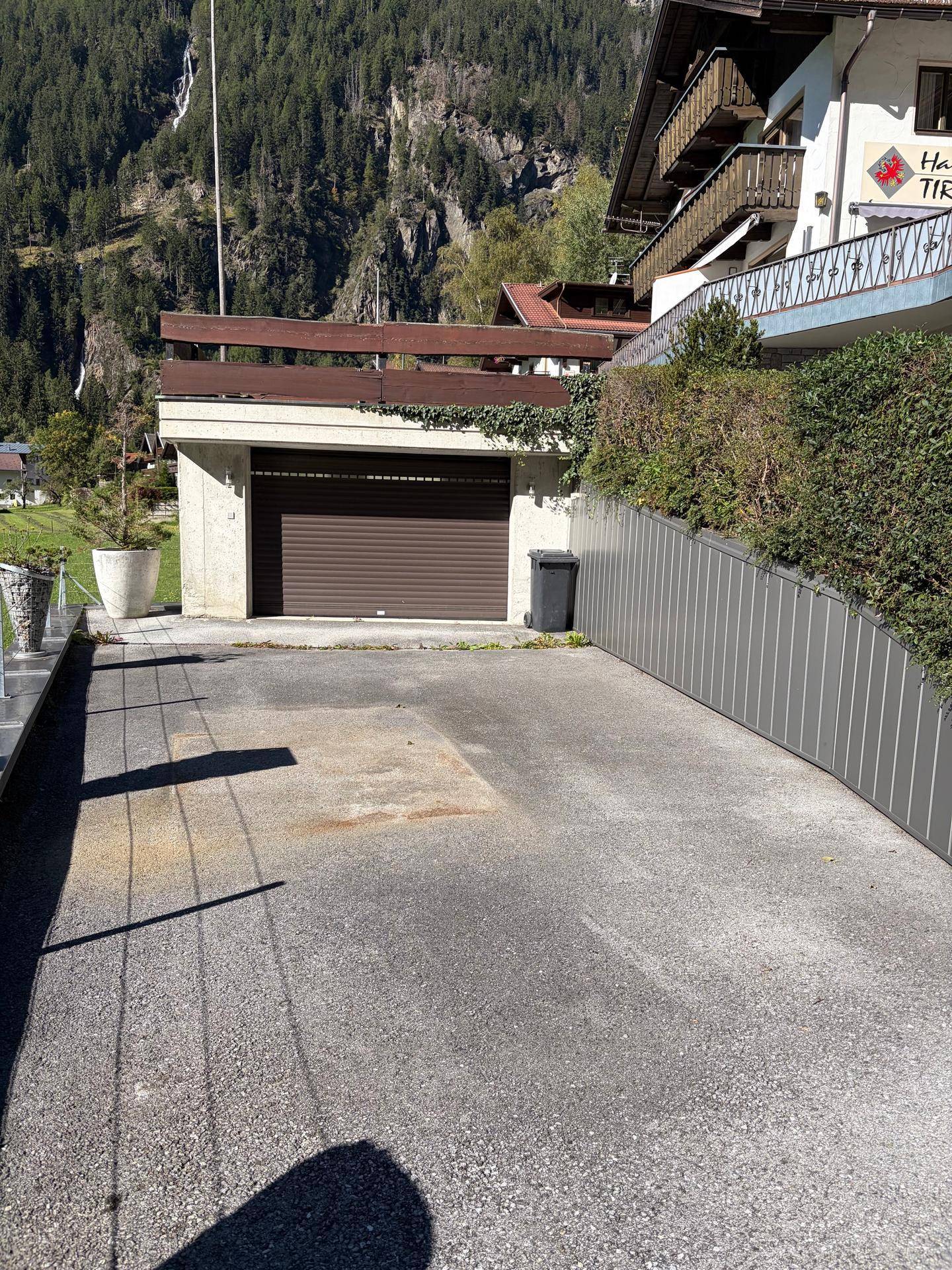 Einfahrt und Garage mit Rolltor vor einer bergigen Kulisse.