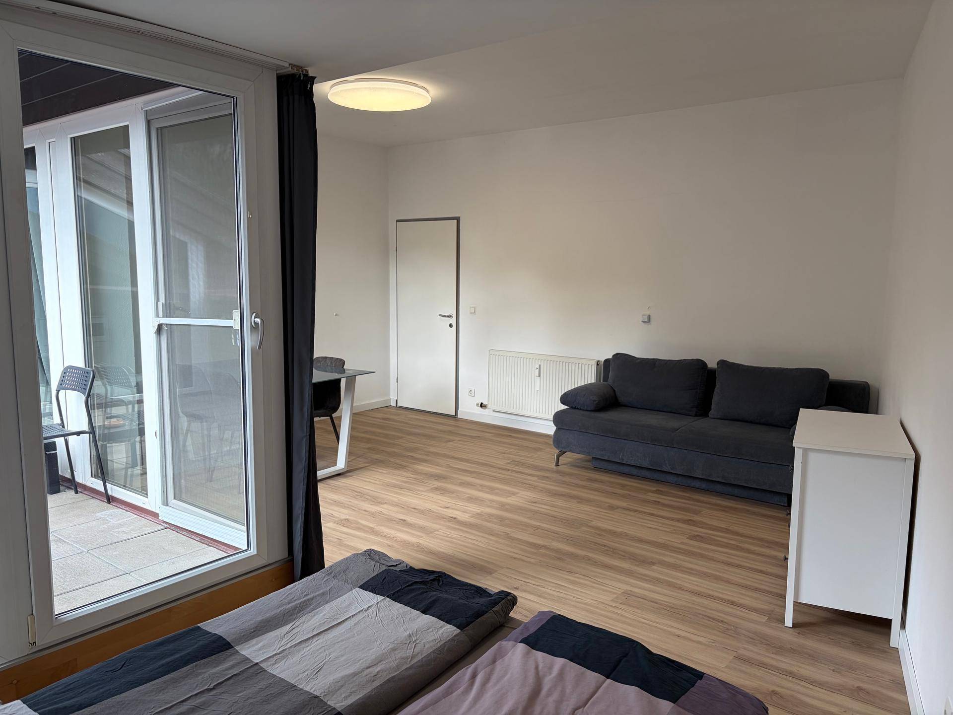 Helles Schlafzimmer mit Zugang zu einem Balkon, ausgestattet mit einem Sofa und einem Schreibtisch.