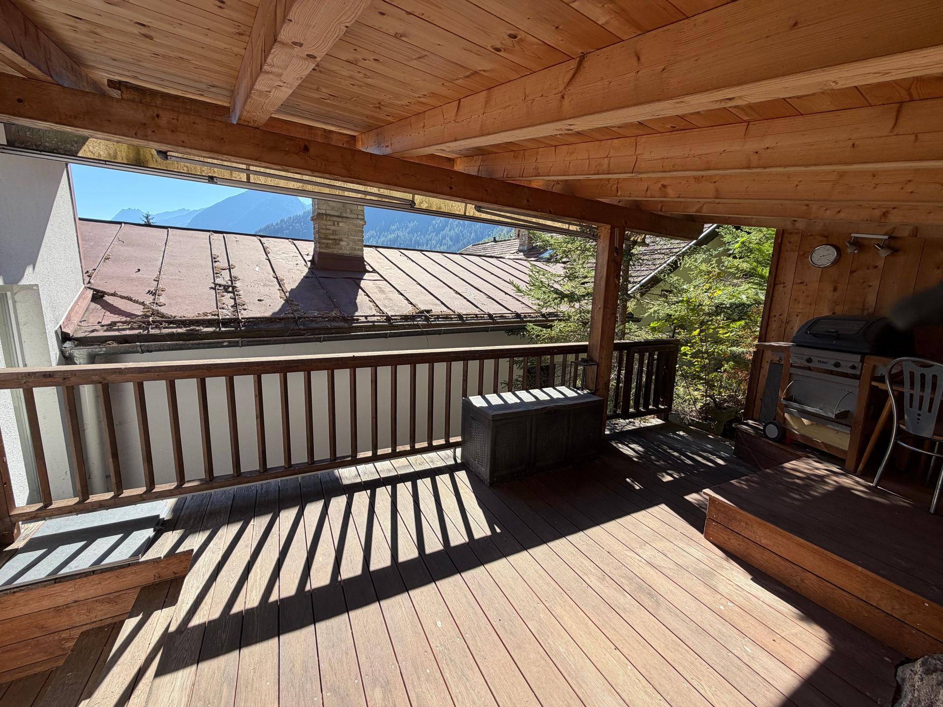 Überdachte Holzterrasse mit Bergblick und Grillbereich, ideal für entspannte Stunden.