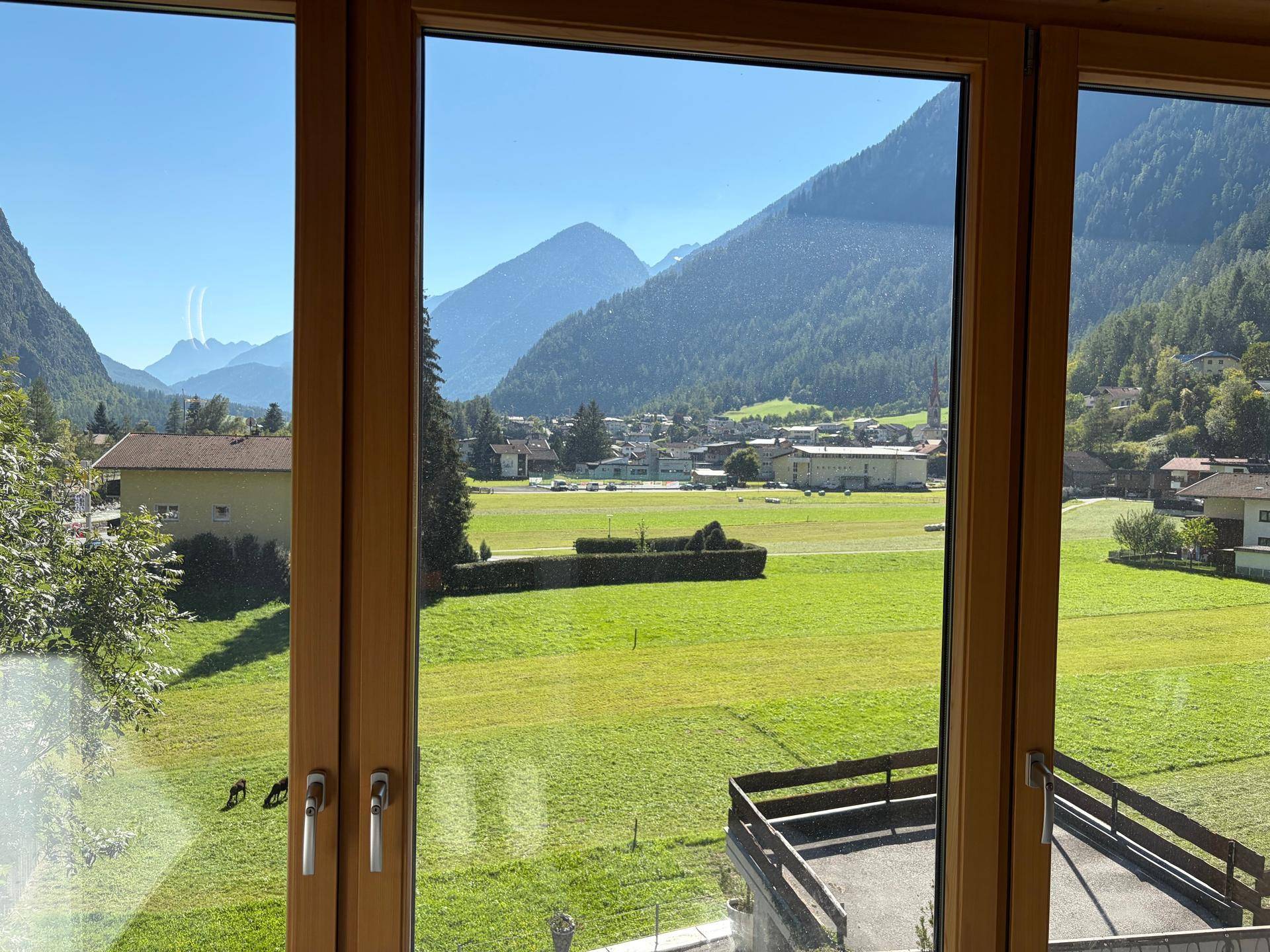 Weitblick aus dem Fenster über eine grüne Landschaft mit Bergen im Hintergrund.