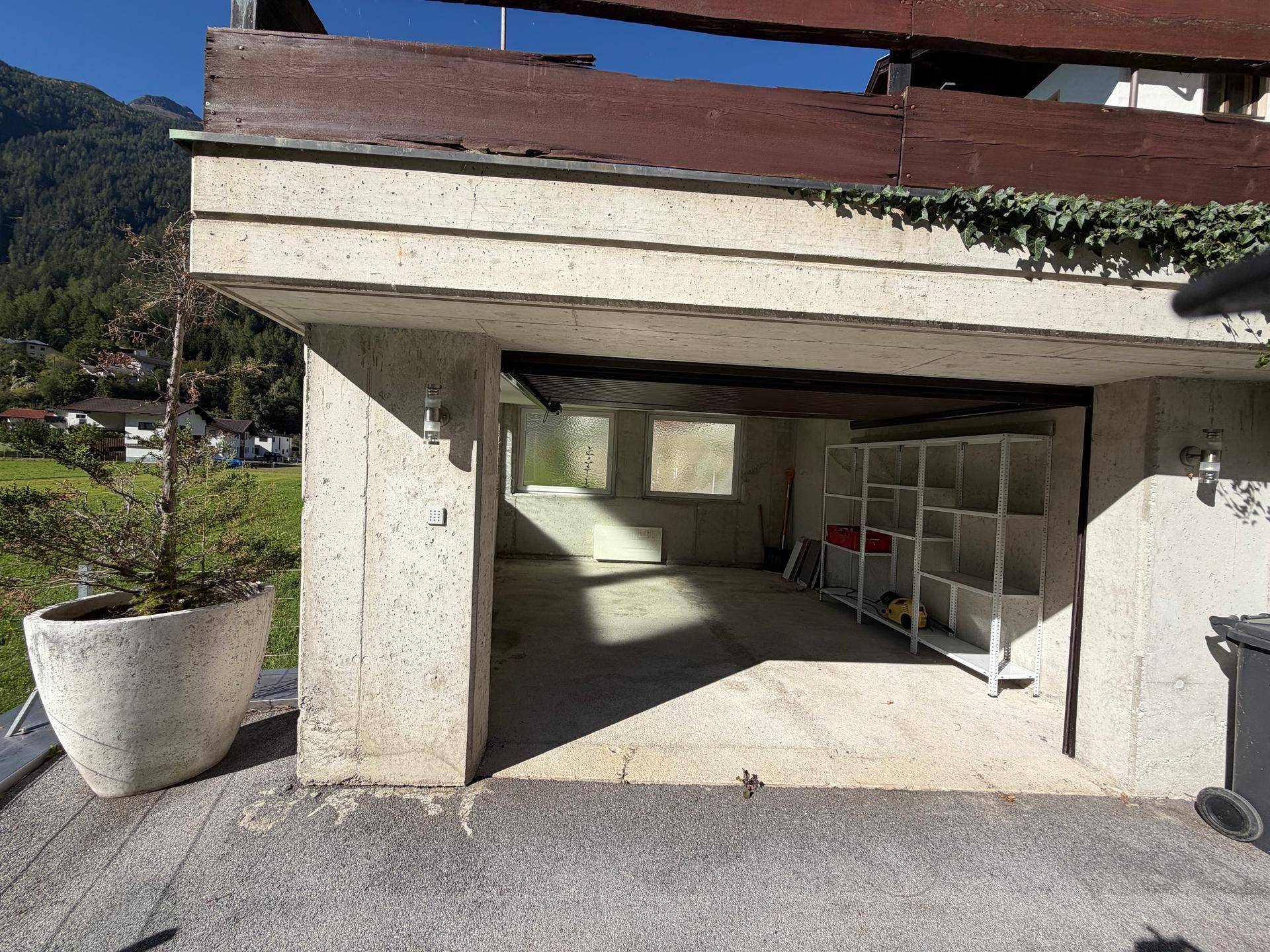 Geräumige Garage mit Betonboden und Regalen für zusätzlichen Stauraum.