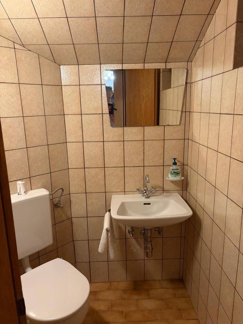Kleines Gäste-WC mit Toilette, Waschbecken und durchgängigen braunen Fliesen.