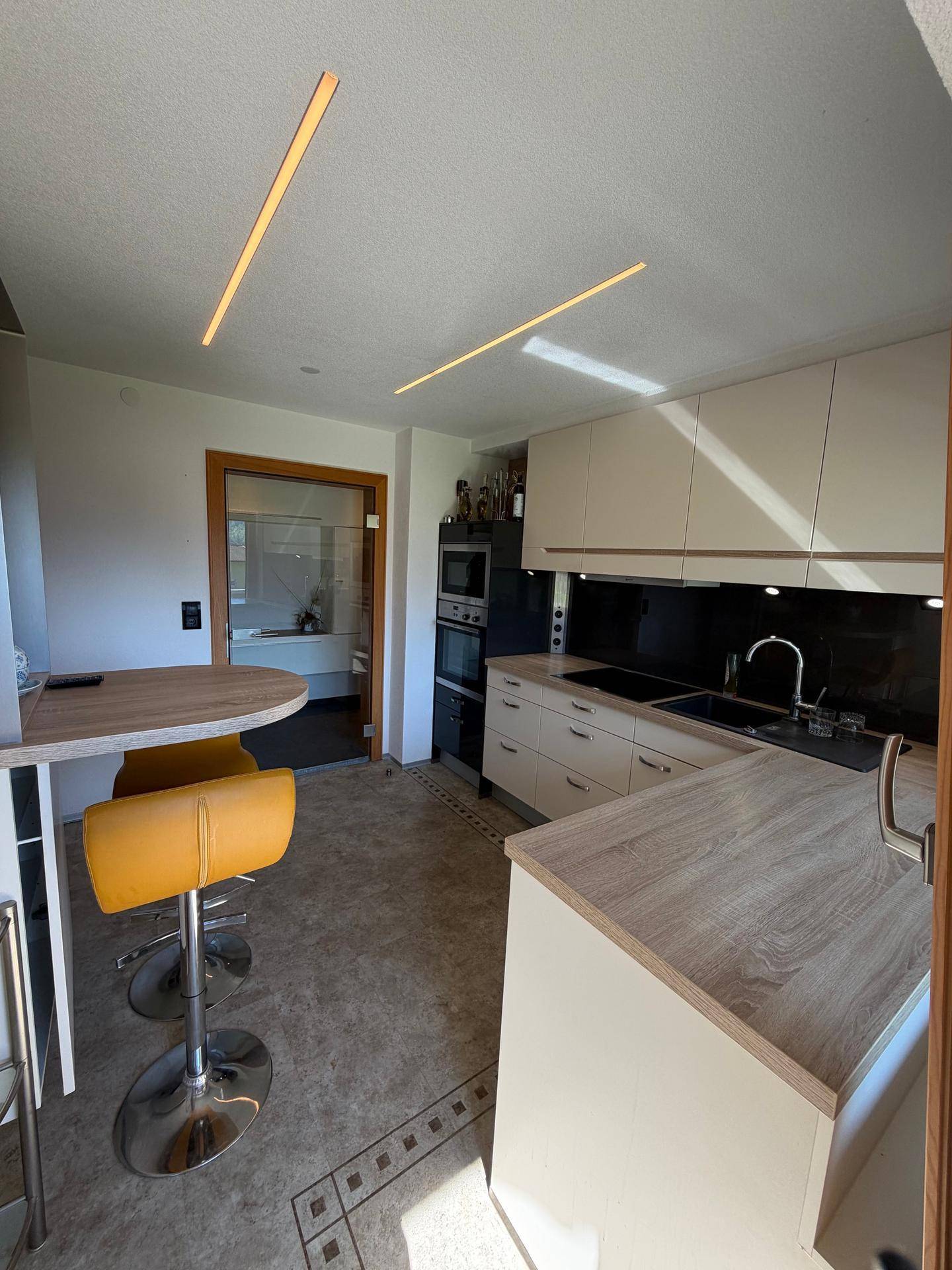 Moderne Küche mit heller Arbeitsplatte, Frühstücksbar und integrierten Geräten.