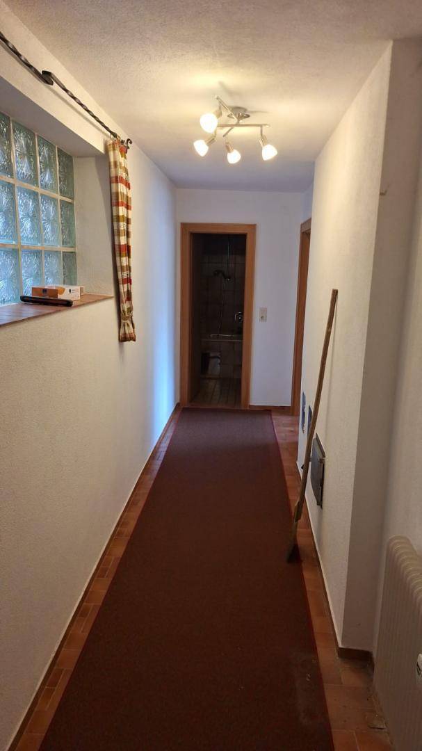 Langer Flur mit Teppichläufer, weißen Wänden und einem Fenster aus Glasbausteinen.