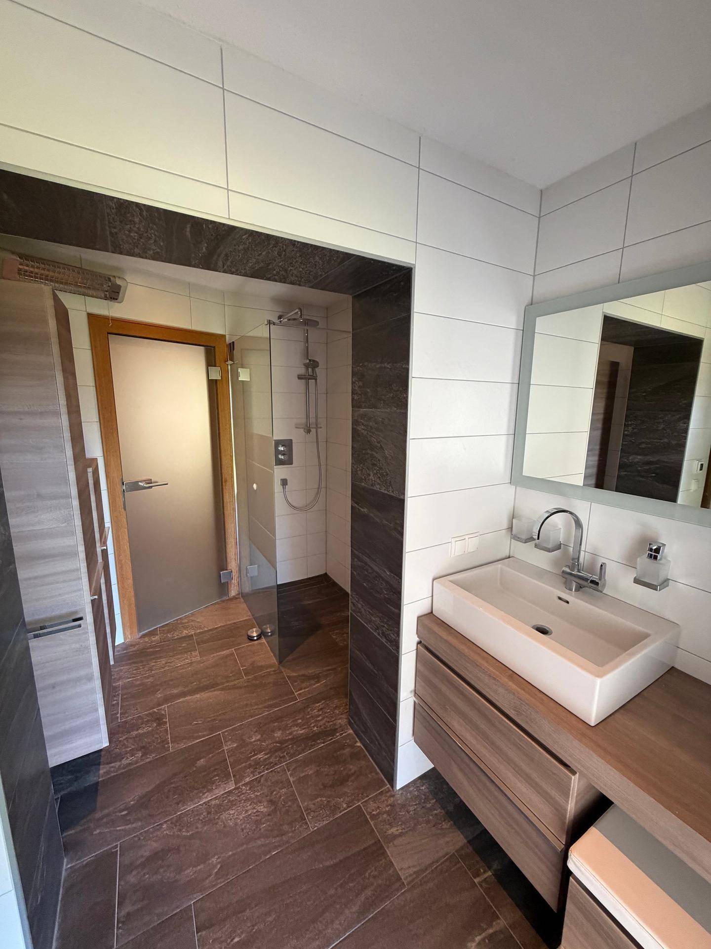 Modernes Badezimmer mit begehbarer Dusche, Einzelwaschbecken und dunklen Fliesen.