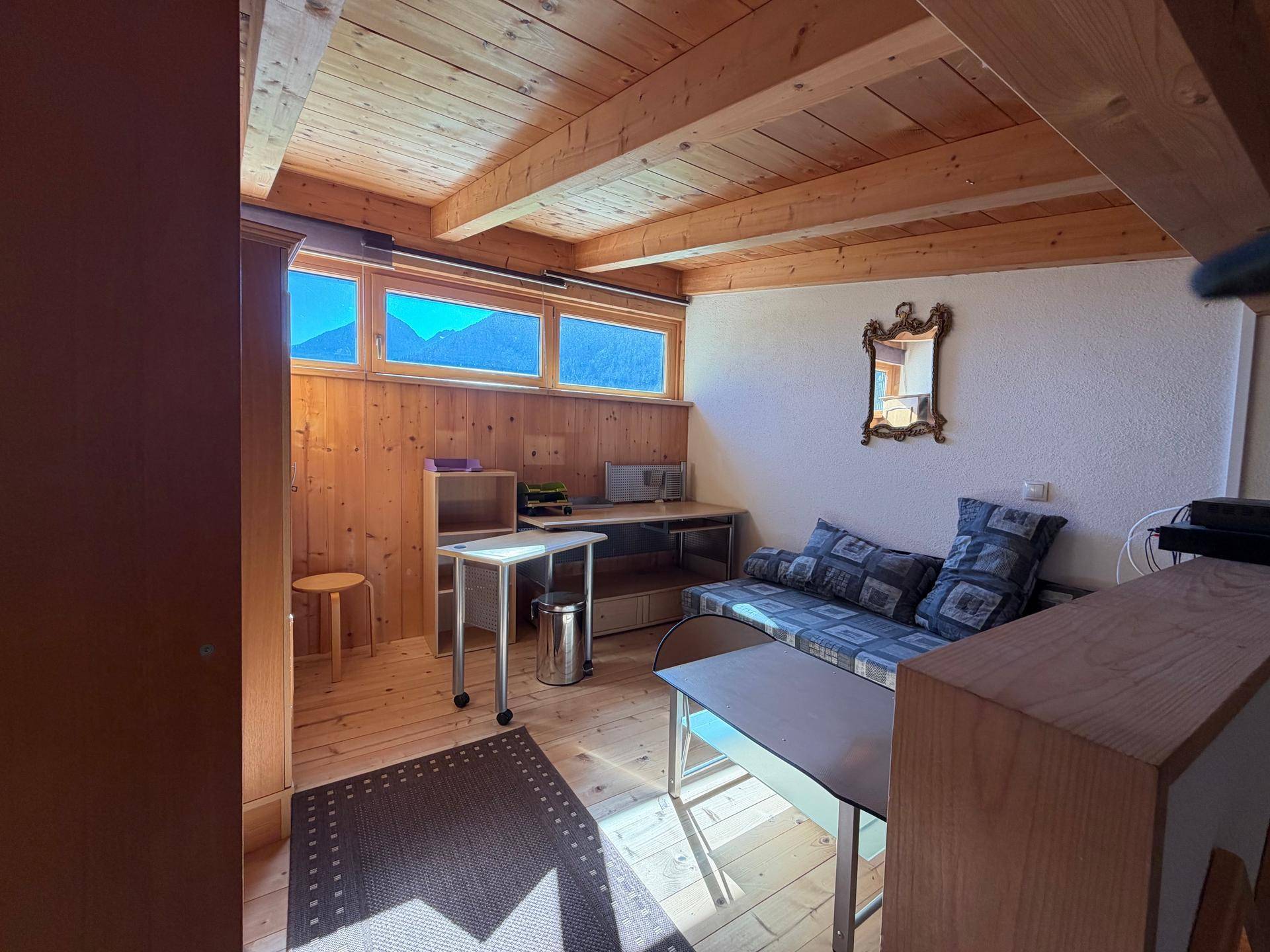 Gemütlicher Wohnraum im alpinen Stil mit Holzverkleidung, Sofa und Bergblick durch die Fenster.